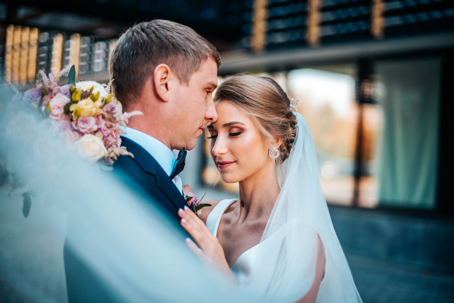 Romantic wedding portrait showing intimate moment between couple in soft blue tones.
