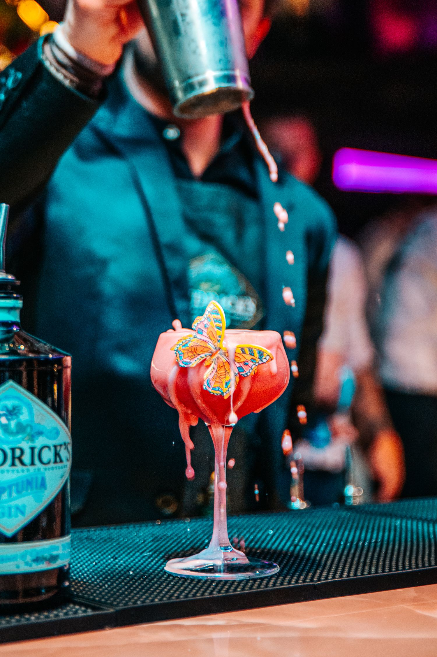 Colorful cocktails being prepared on a bar counter with professional garnishes.