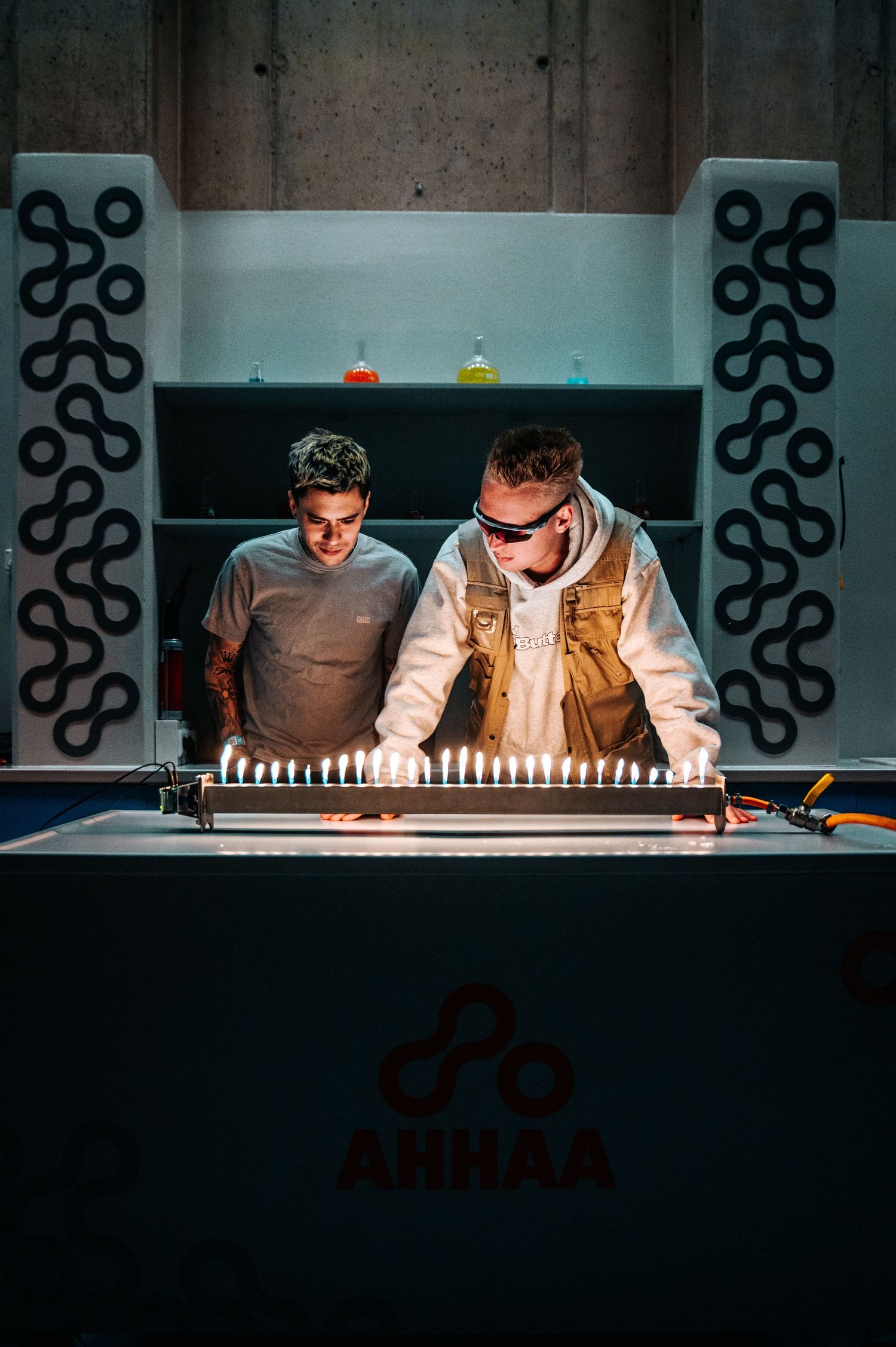 DJs performing behind a minimalist booth with geometric wall decorations.
