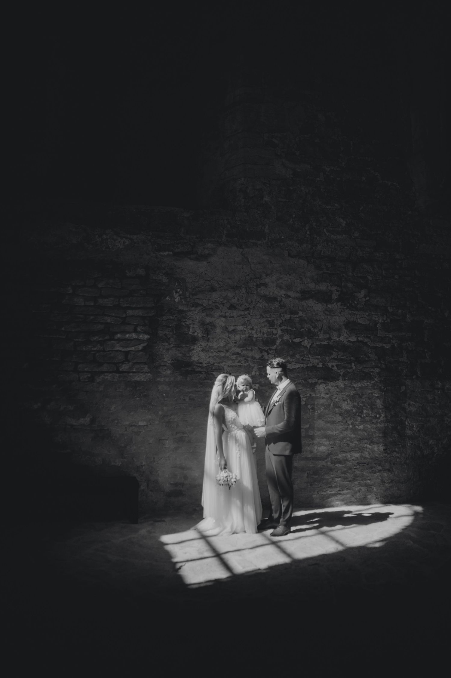 A dramatic black and white photo of a couple in an old stone building with light streaming through windows.