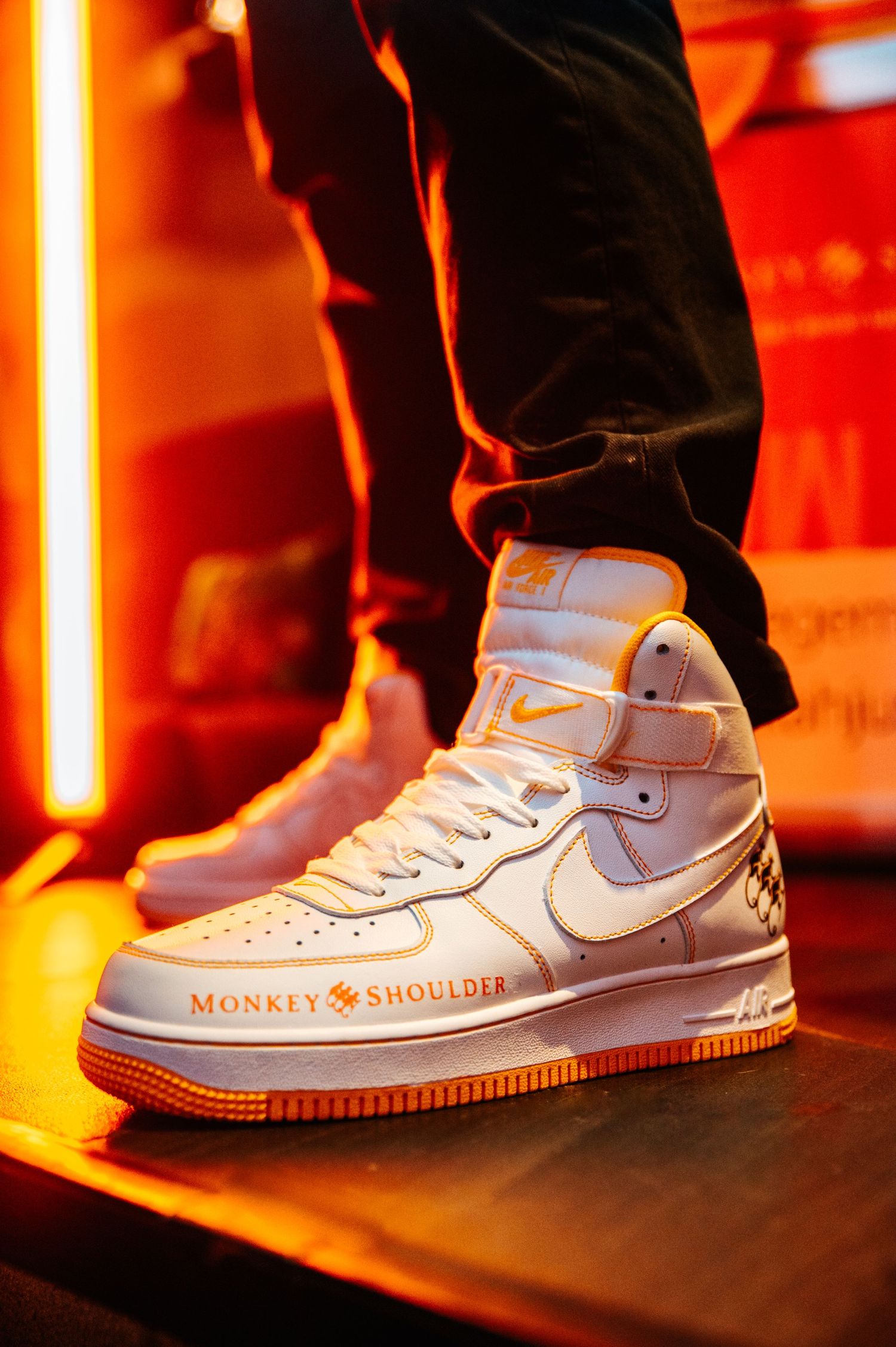 White Nike Air Force 1 sneakers illuminated by orange lighting at an event.