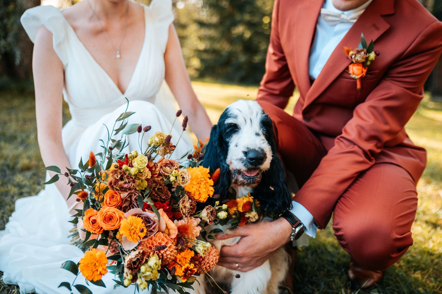 Wedding couple holds vibrant orange and burgundy floral bouquet with autumn colors against maroon suit details.