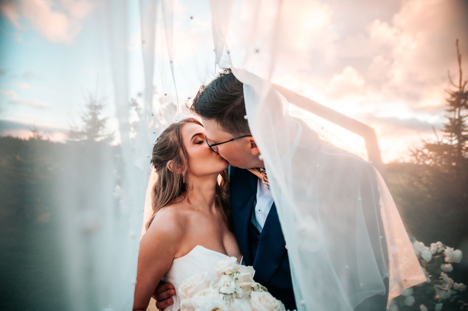 Romantic wedding moment captured under flowing white fabric with soft lighting and dreamy atmosphere.