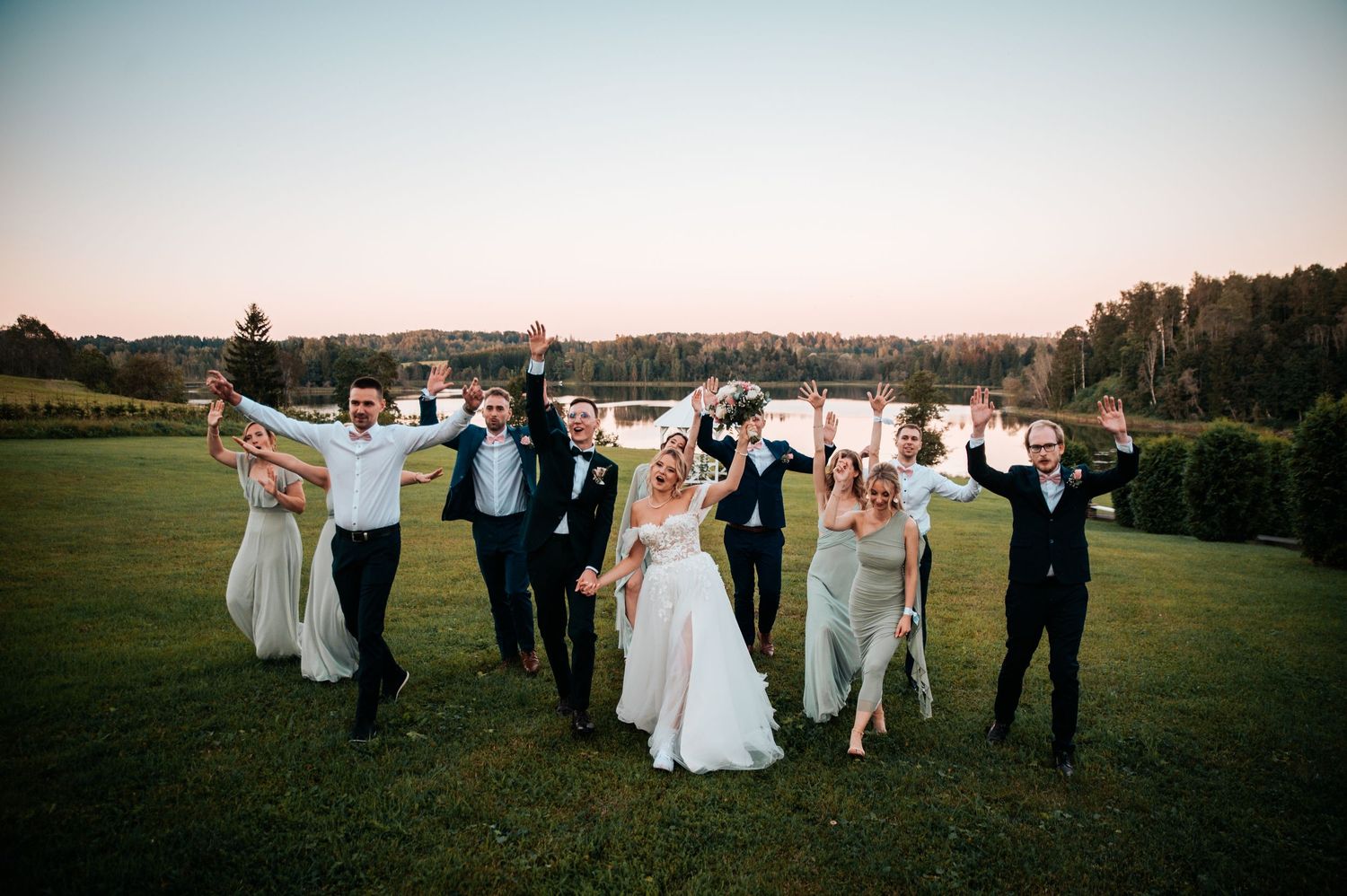 Wedding party celebrates outdoors holding letter signs against sunset sky.