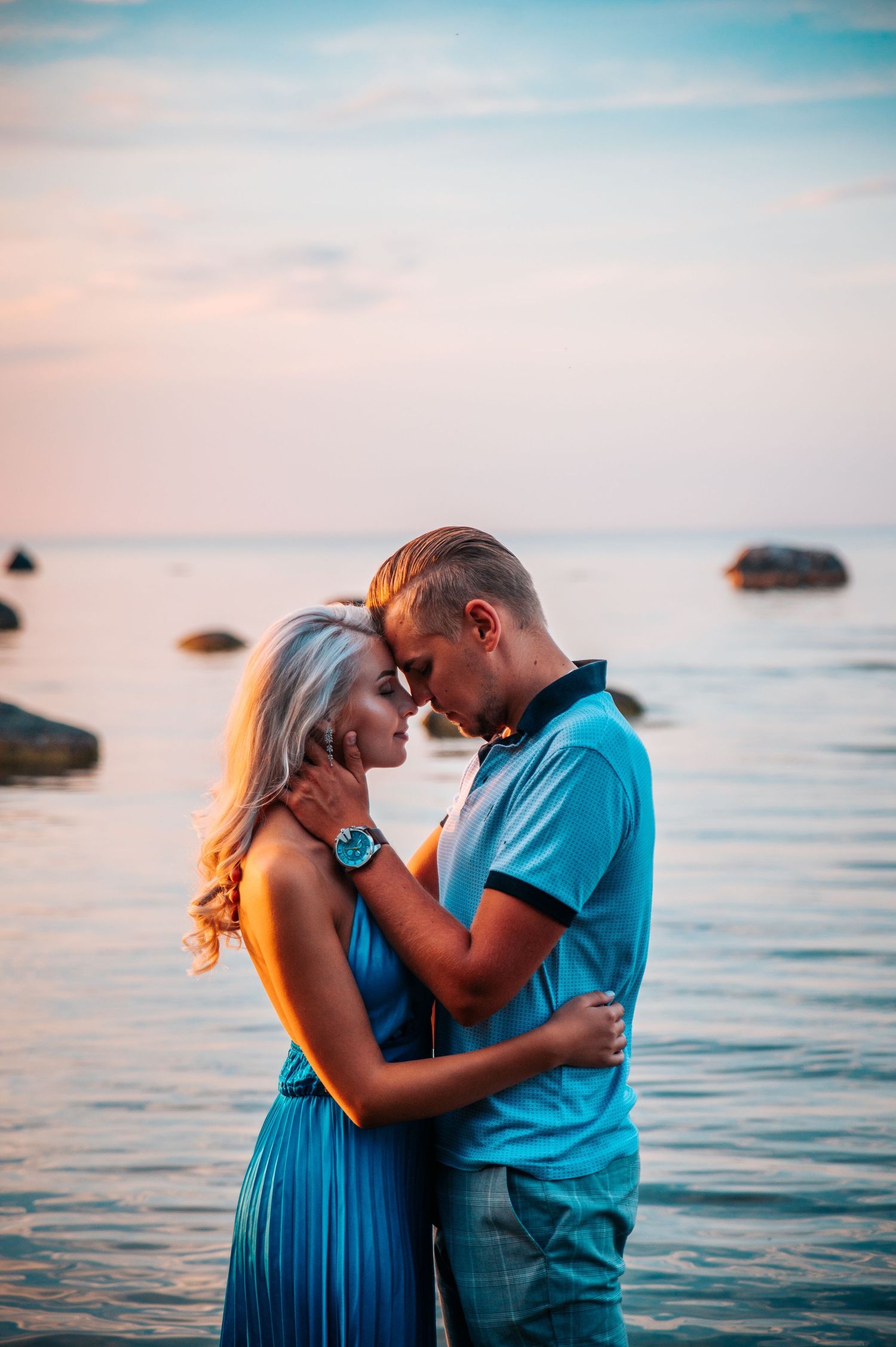 A romantic couple shares tender moments at sunset by the ocean in matching blue outfits.
