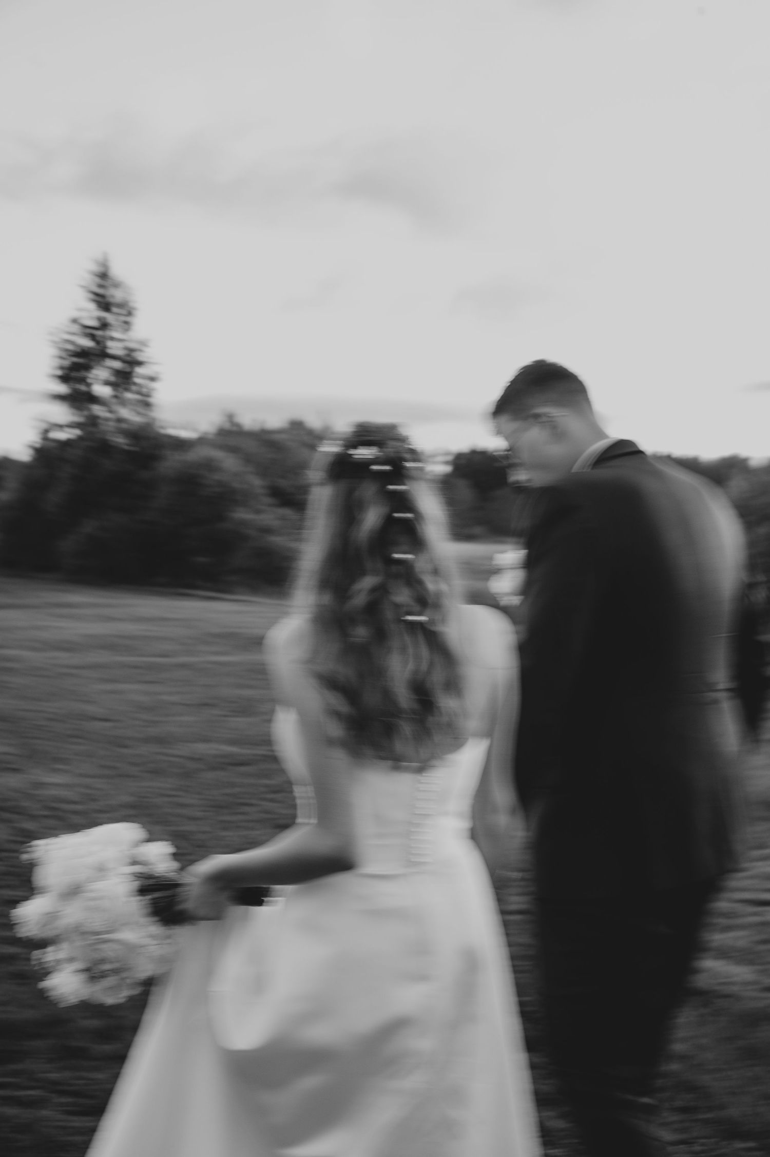 A series of motion blur photos shows a couple walking away in wedding attire across an outdoor field.