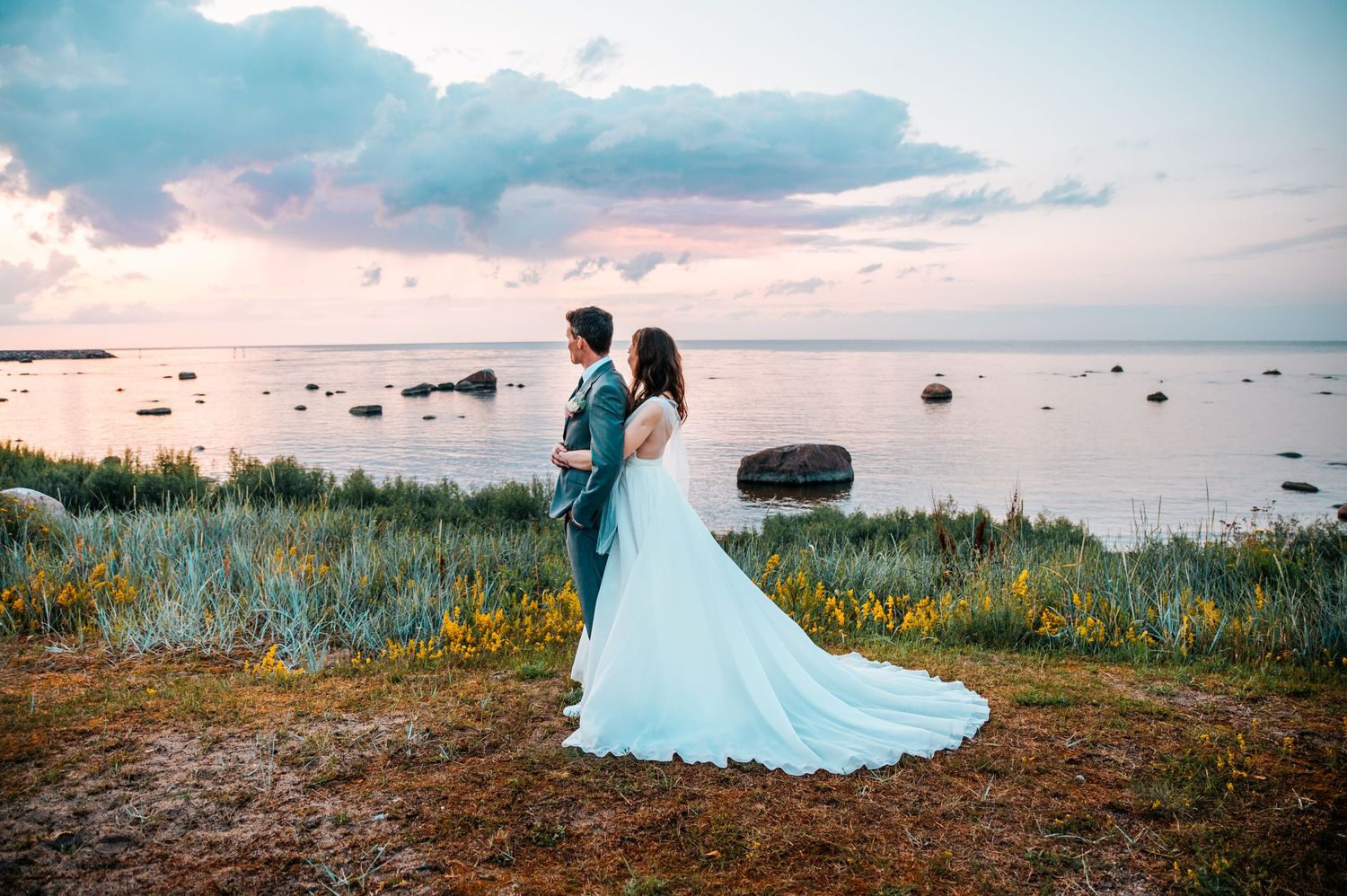 A flowing white wedding dress photographed against a scenic coastal landscape during sunset.