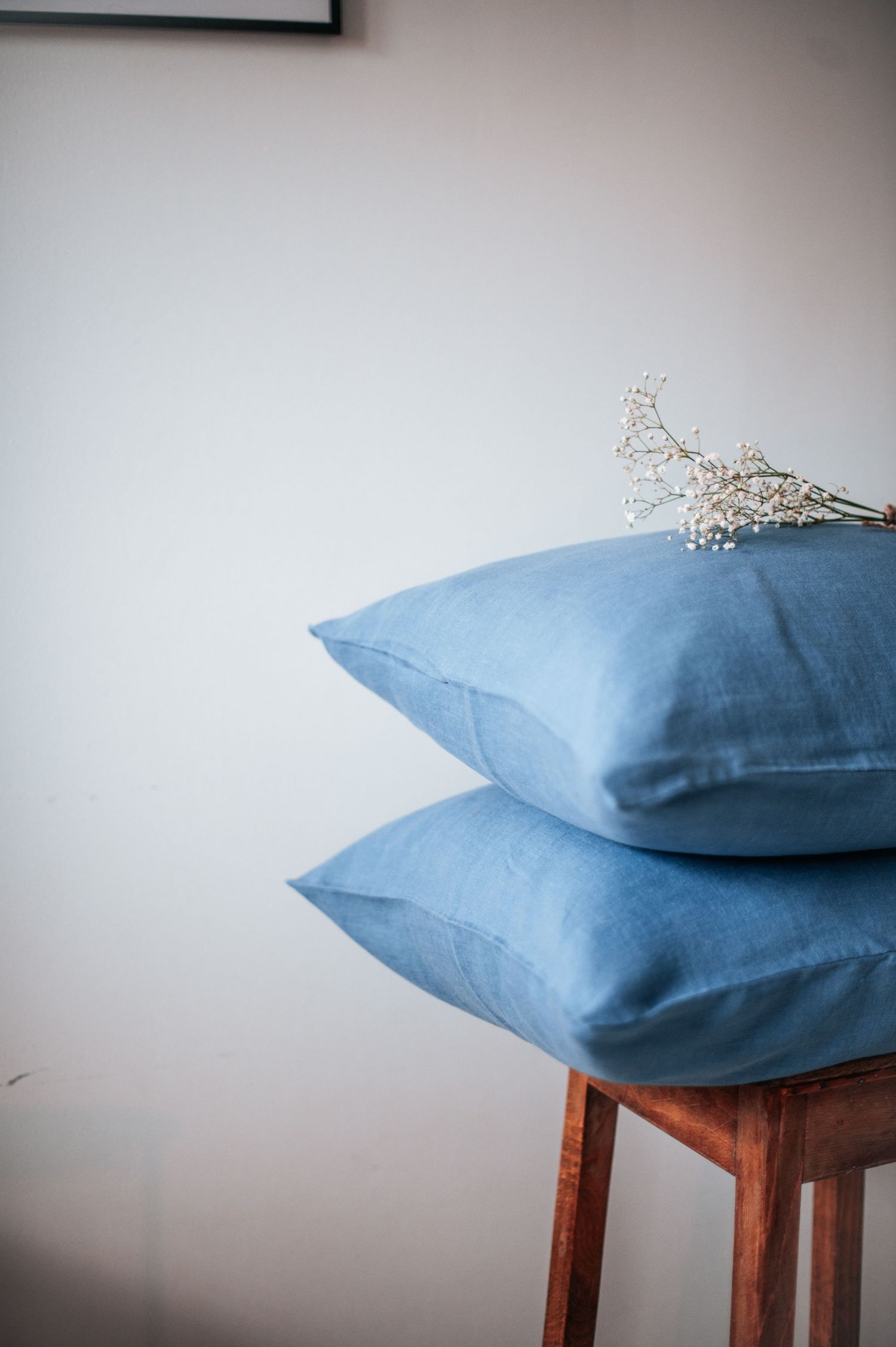 Blue pillows stacked on wooden chair with delicate floral accent.