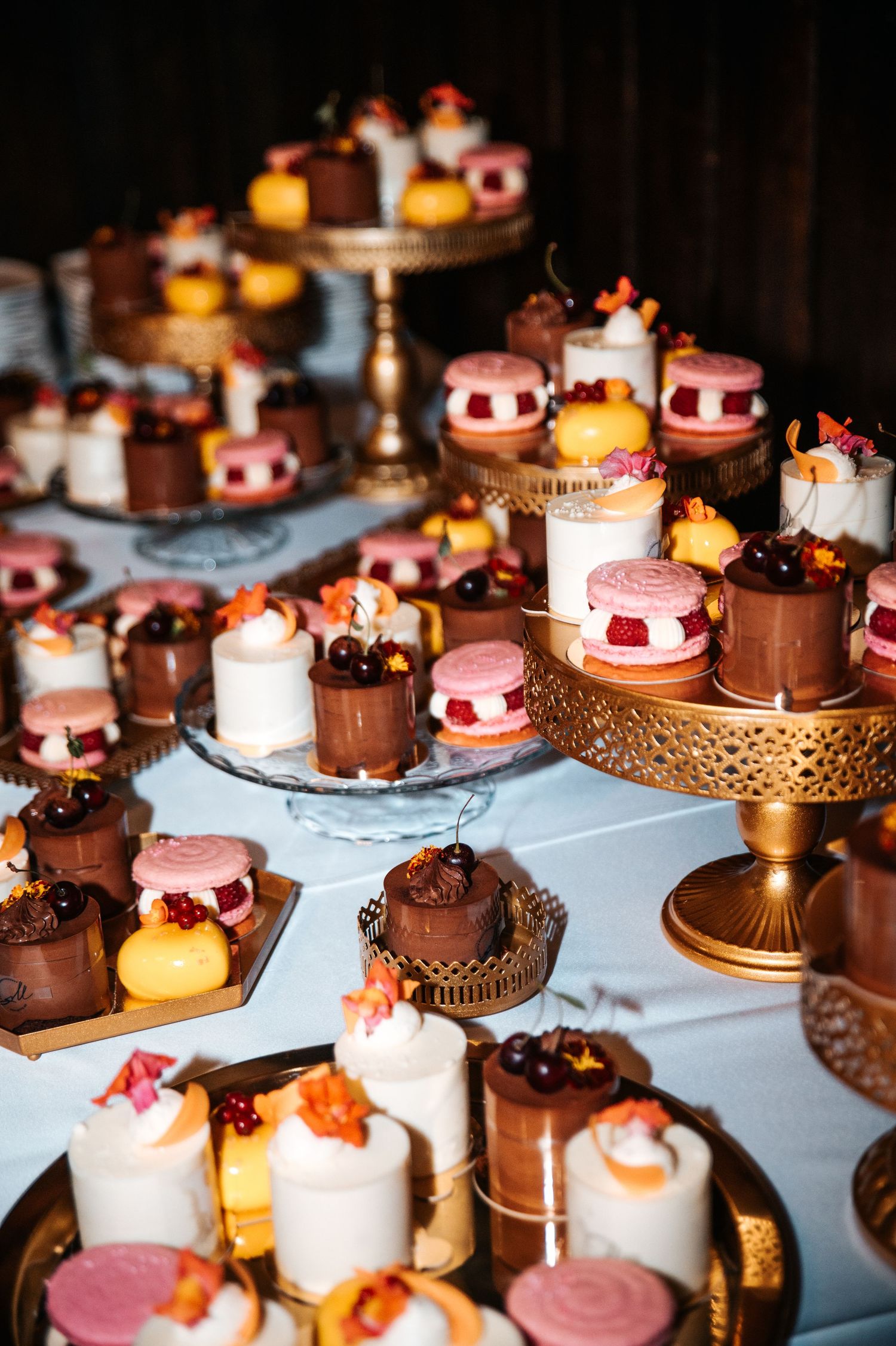 Elegant dessert table with pink and chocolate mini cakes on gold stands.