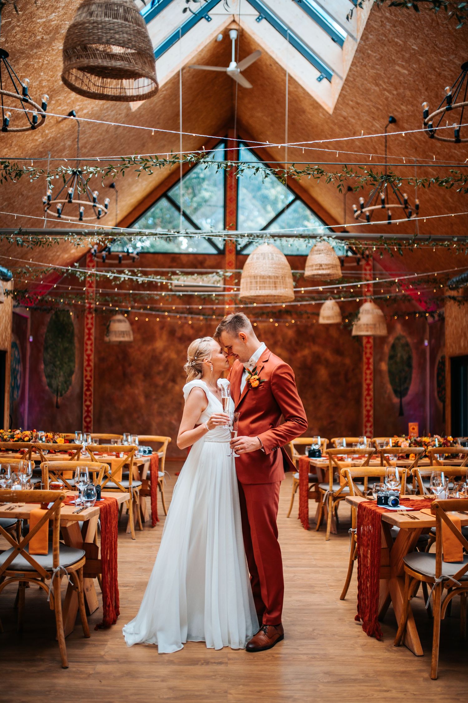 A couple shares an intimate dance moment in a rustic barn venue decorated with string lights and wooden chairs.