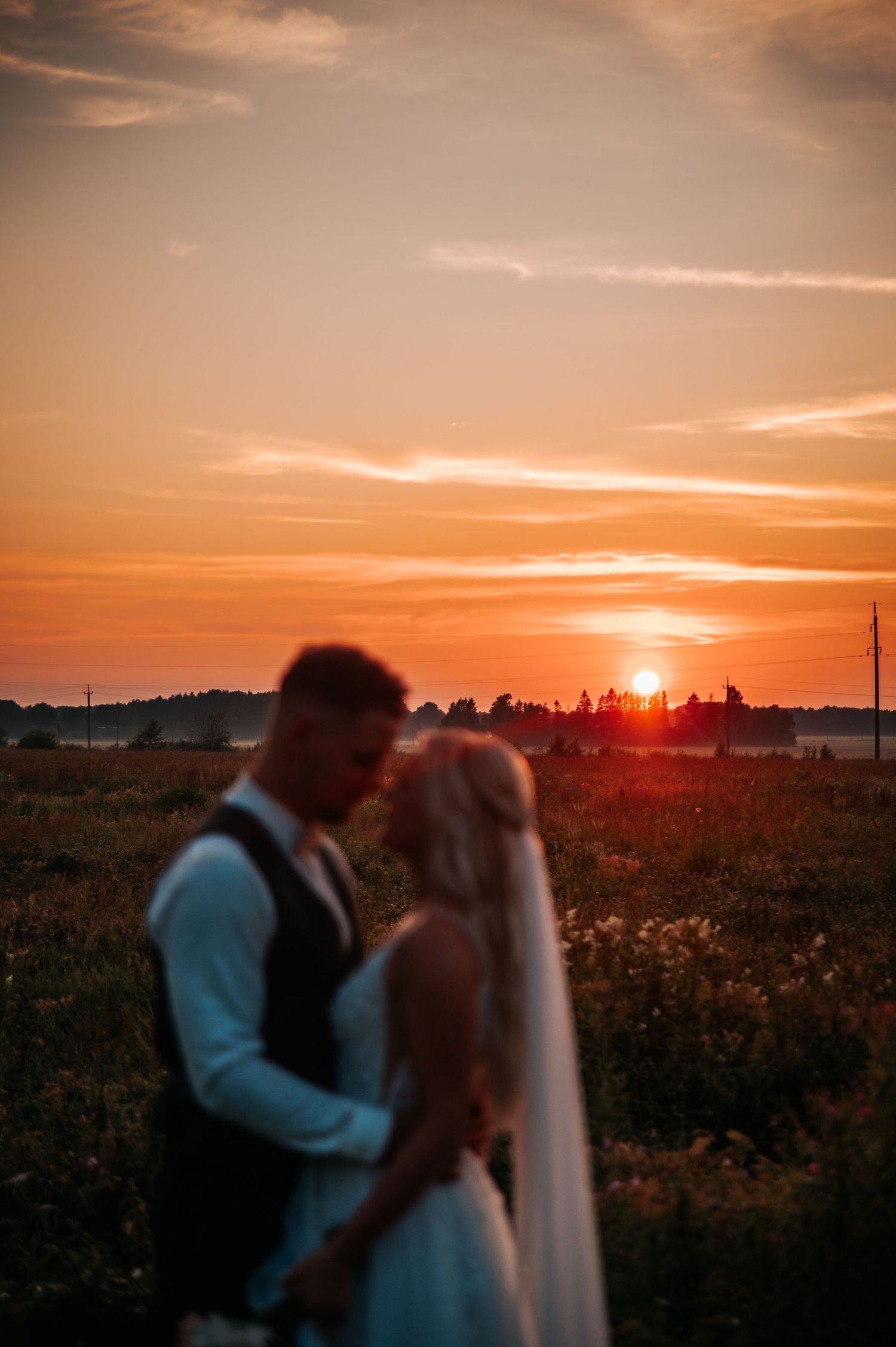 A couple shares a romantic kiss at sunset in a field with golden light streaming through the clouds.