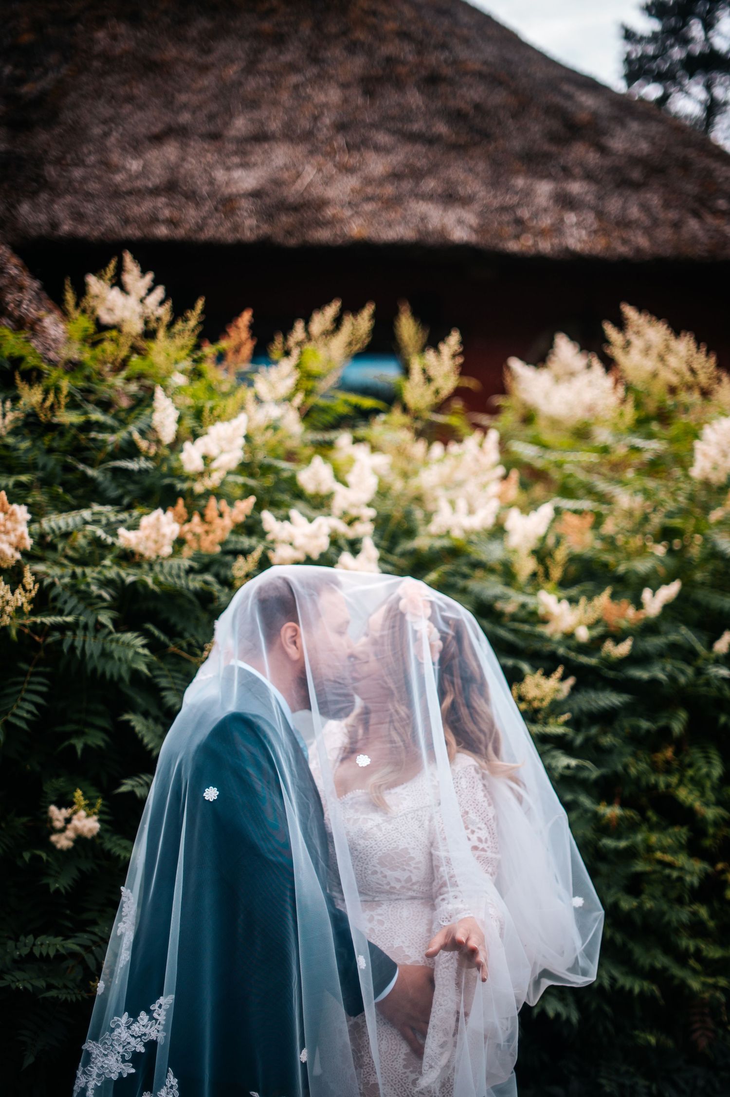 A tender wedding moment captured through delicate veil details against natural foliage.