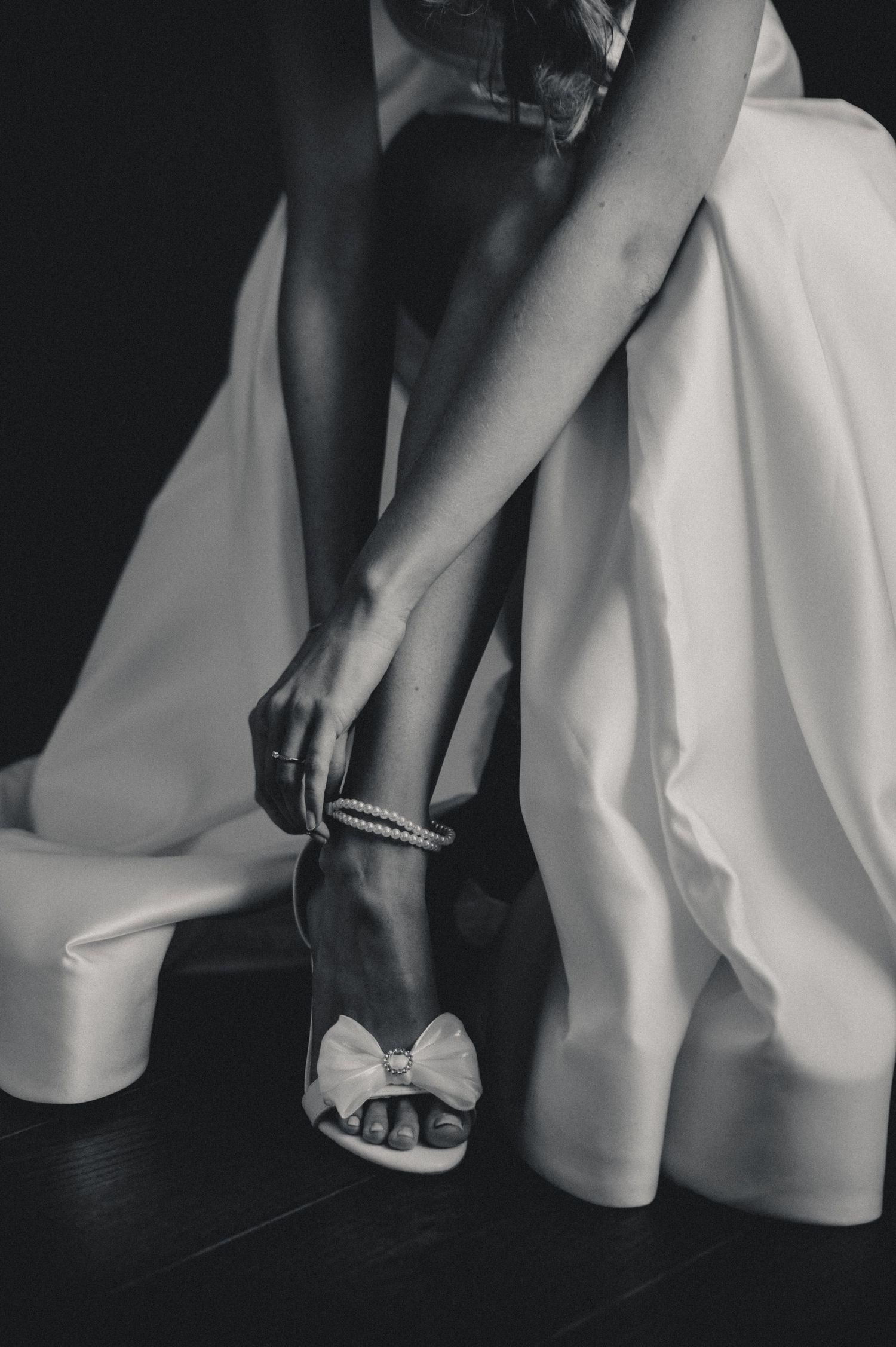 Black and white photo of bride fastening elegant bow wedding shoes.