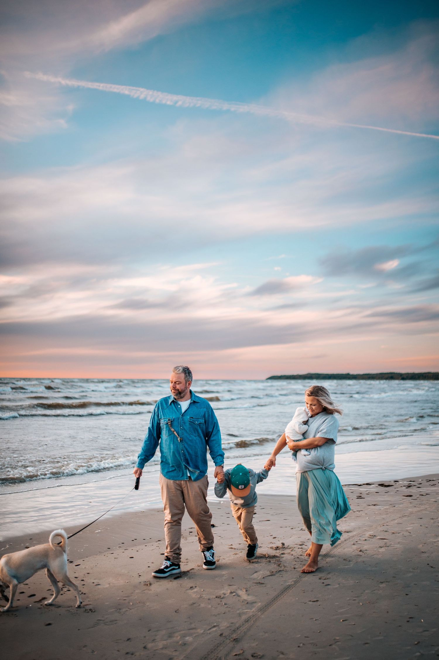 Family and dog enjoying a playful moment together while walking along a scenic beach at sunset.