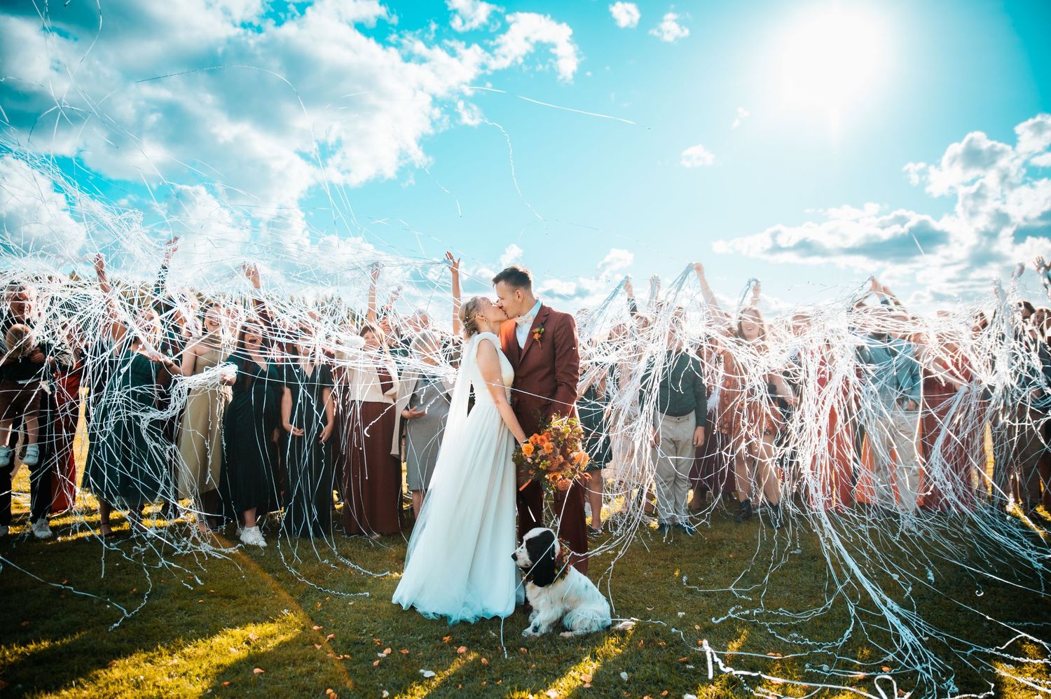 Wedding celebration with guests throwing streamers in golden sunlight.