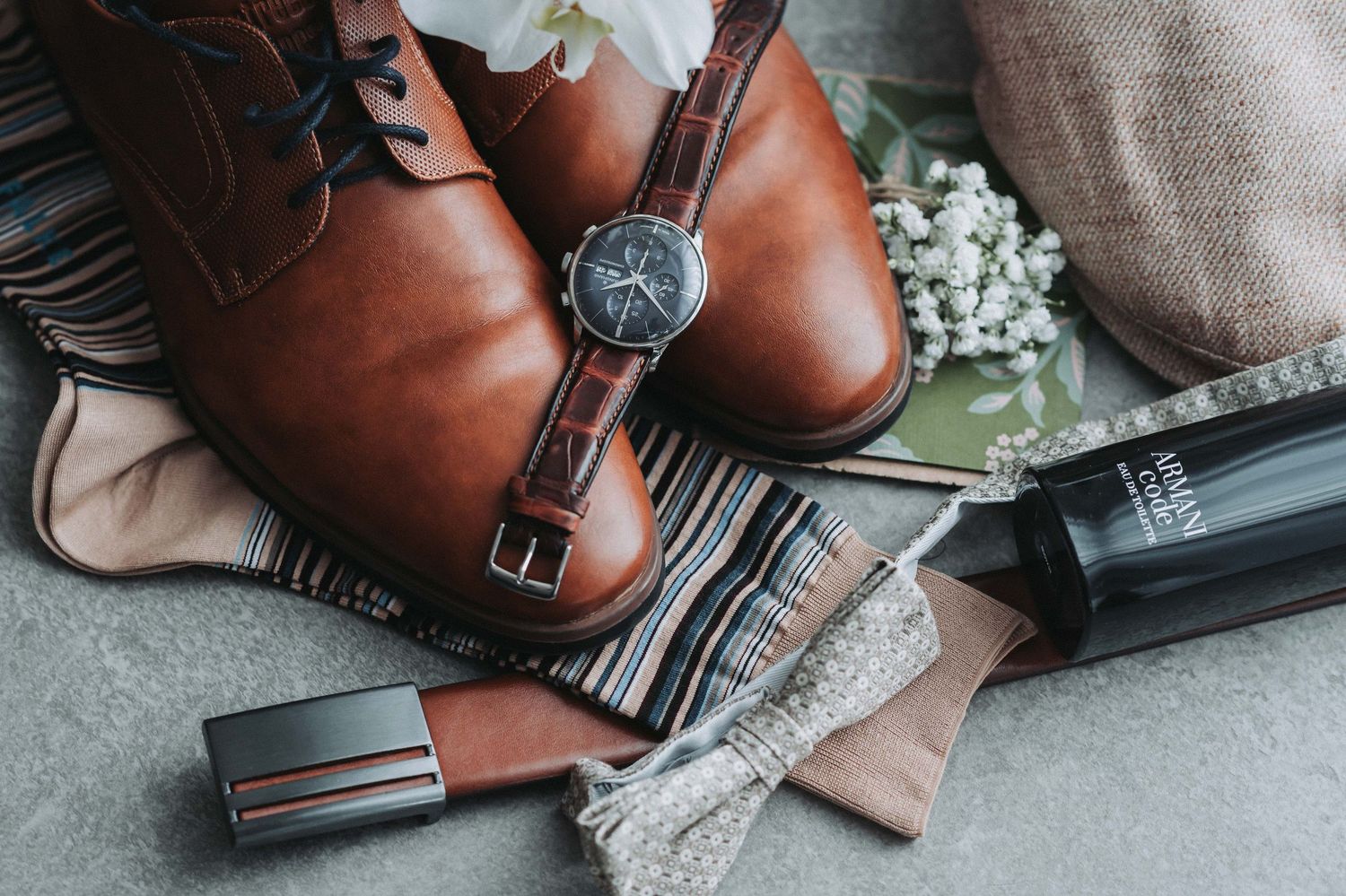 A collection of brown leather shoes and accessories arranged with knit fabrics in a lifestyle flatlay composition.