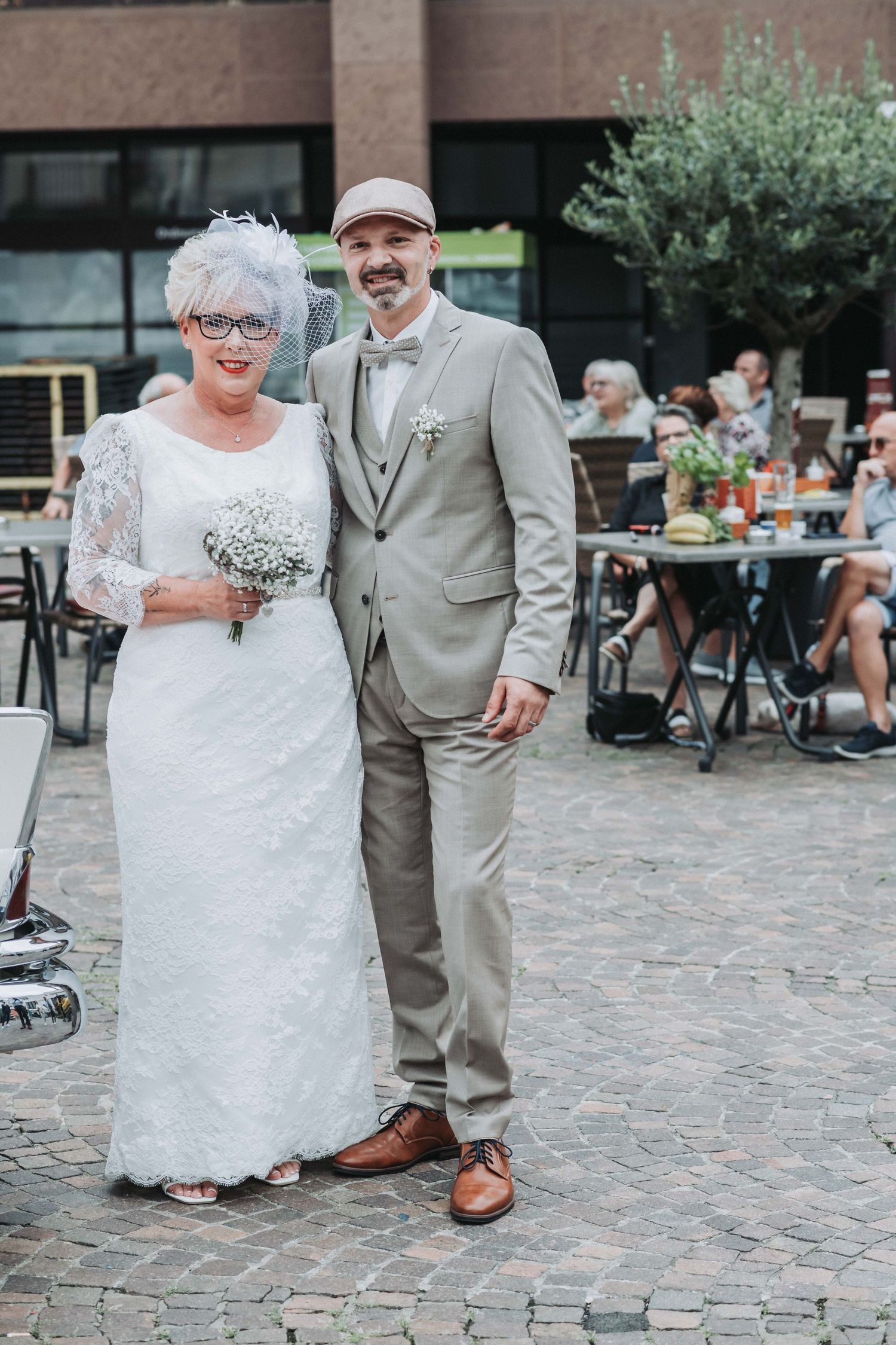 Happy couple celebrates their wedding day with joyful dance moves on a cobblestone courtyard.