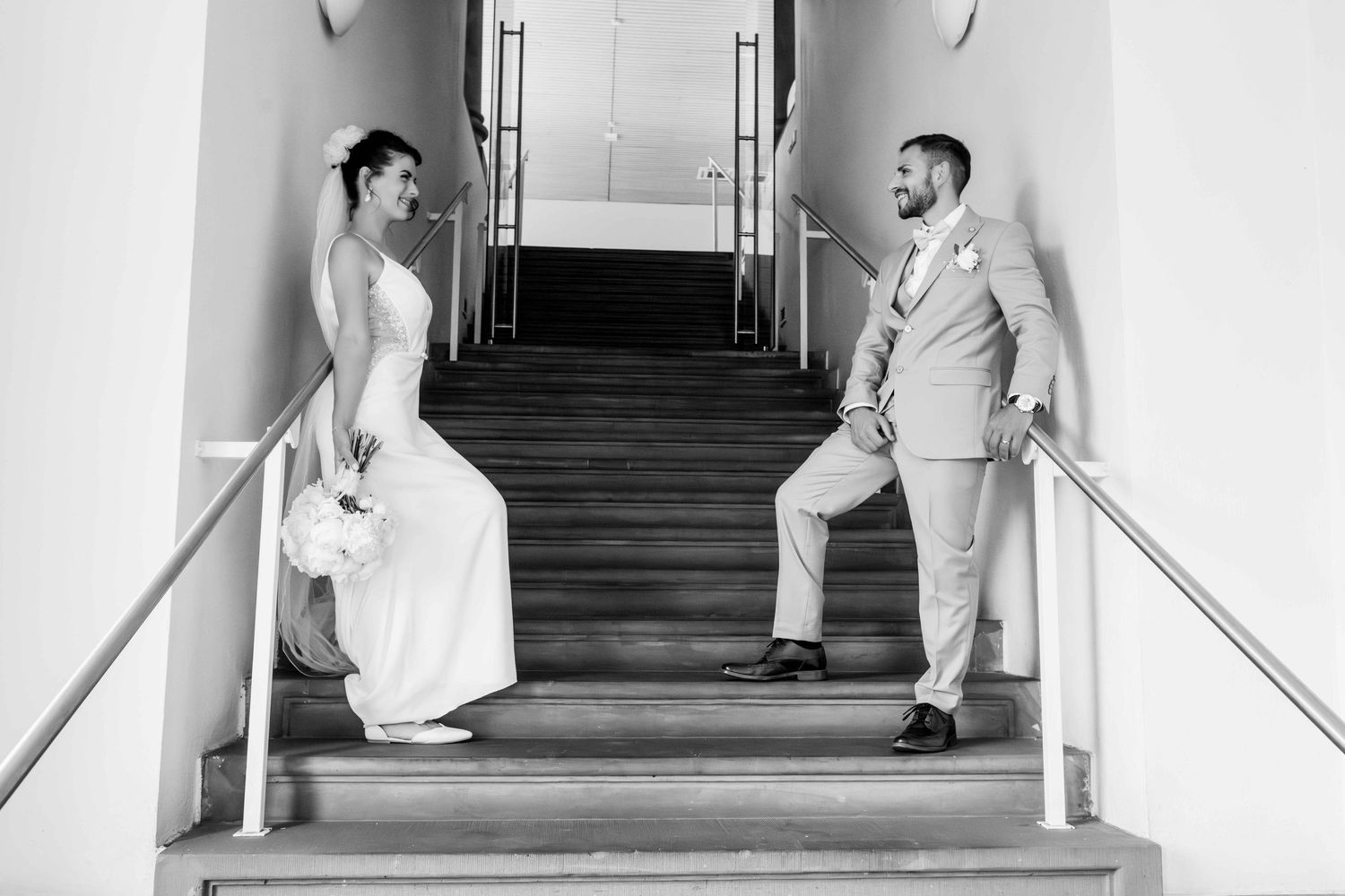 A bride and groom pose playfully on opposite sides of a staircase in black and white.