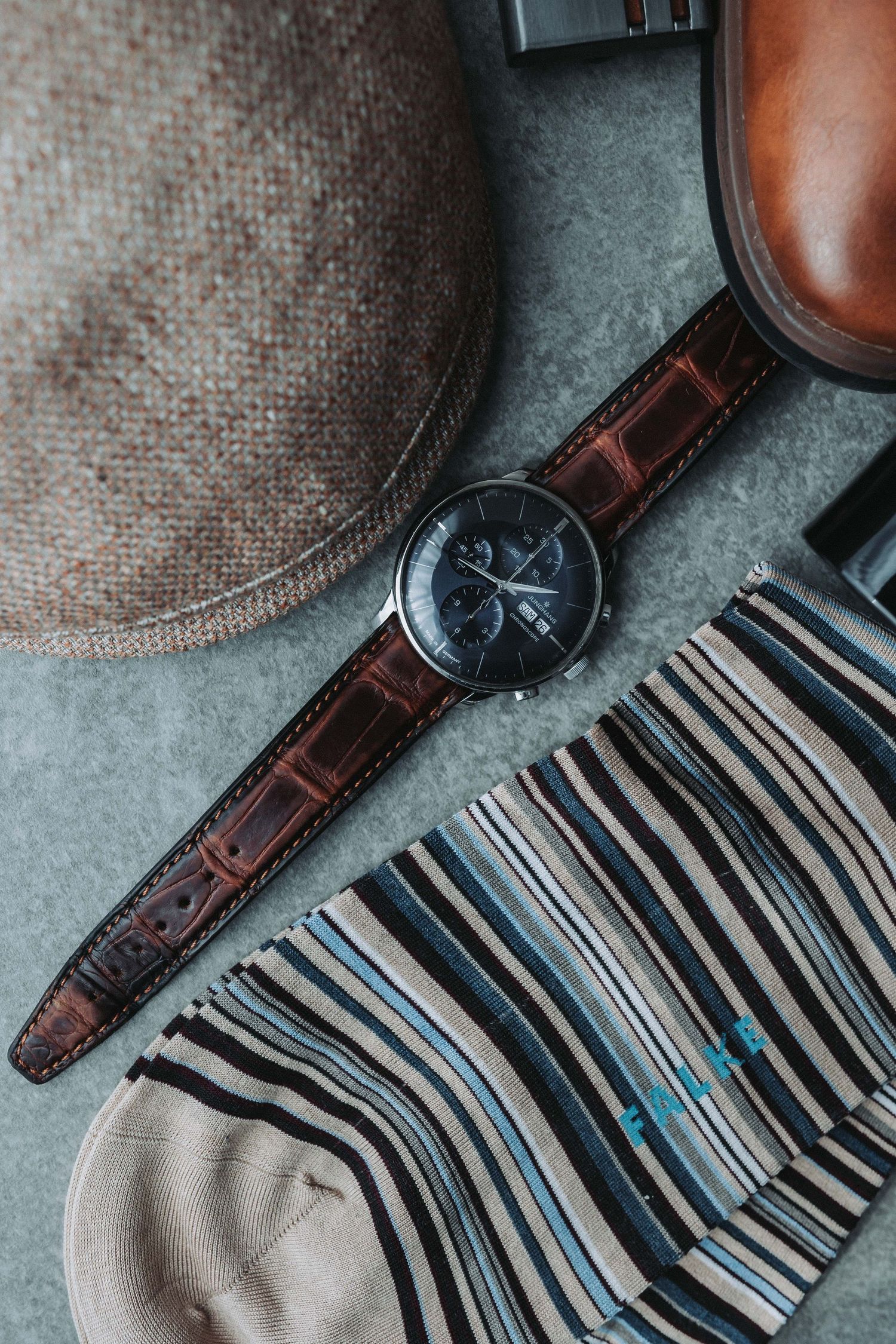 A brown leather watch with black face lies on a striped fabric background in muted tones.