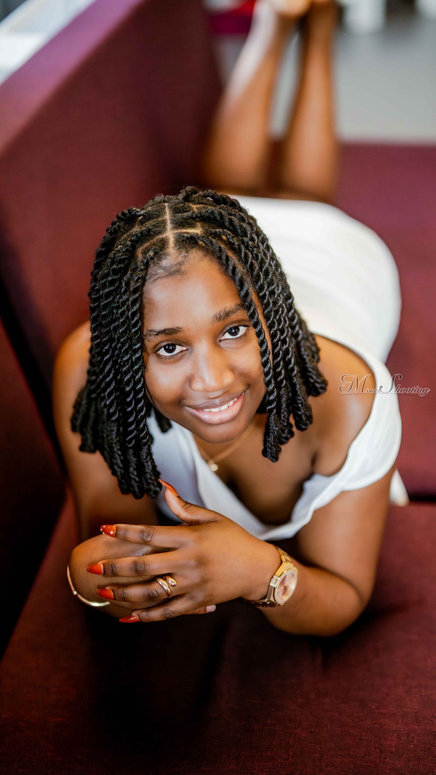 Portrait series showing a person with twisted braids in a white top laying on a burgundy surface.
