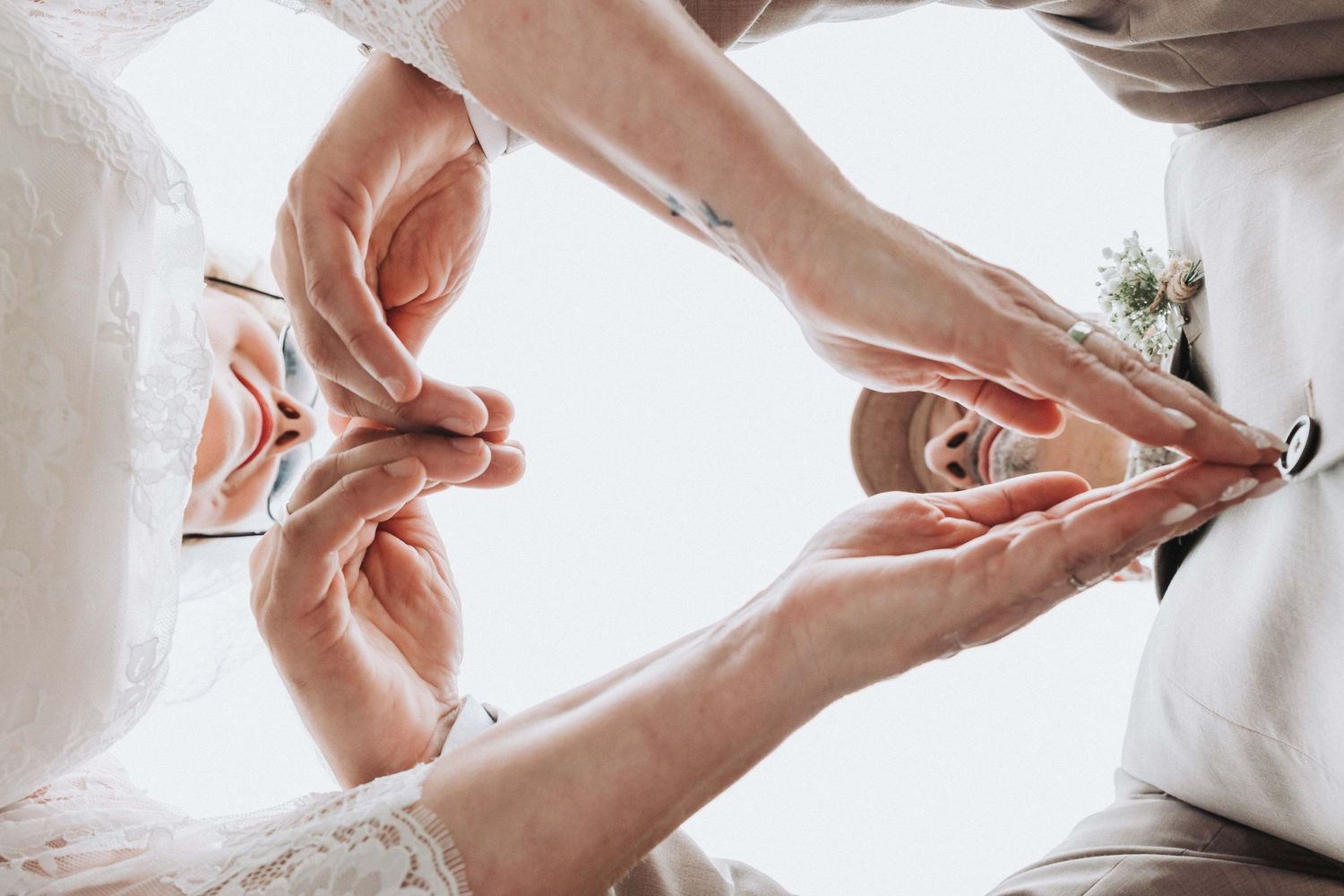 Hands holding and adjusting a white wedding dress in natural light from above.