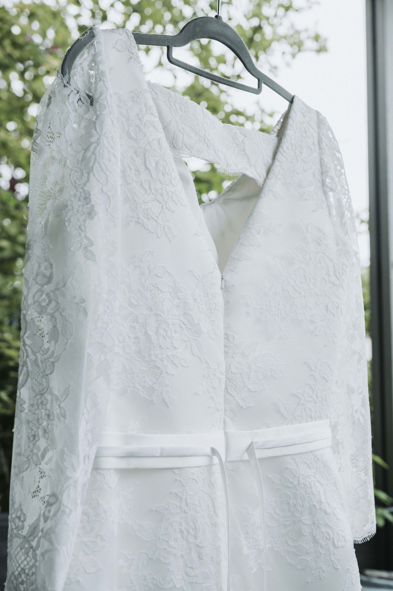 White lace wedding dresses hanging on hangers in a row against a window with natural light filtering through.
