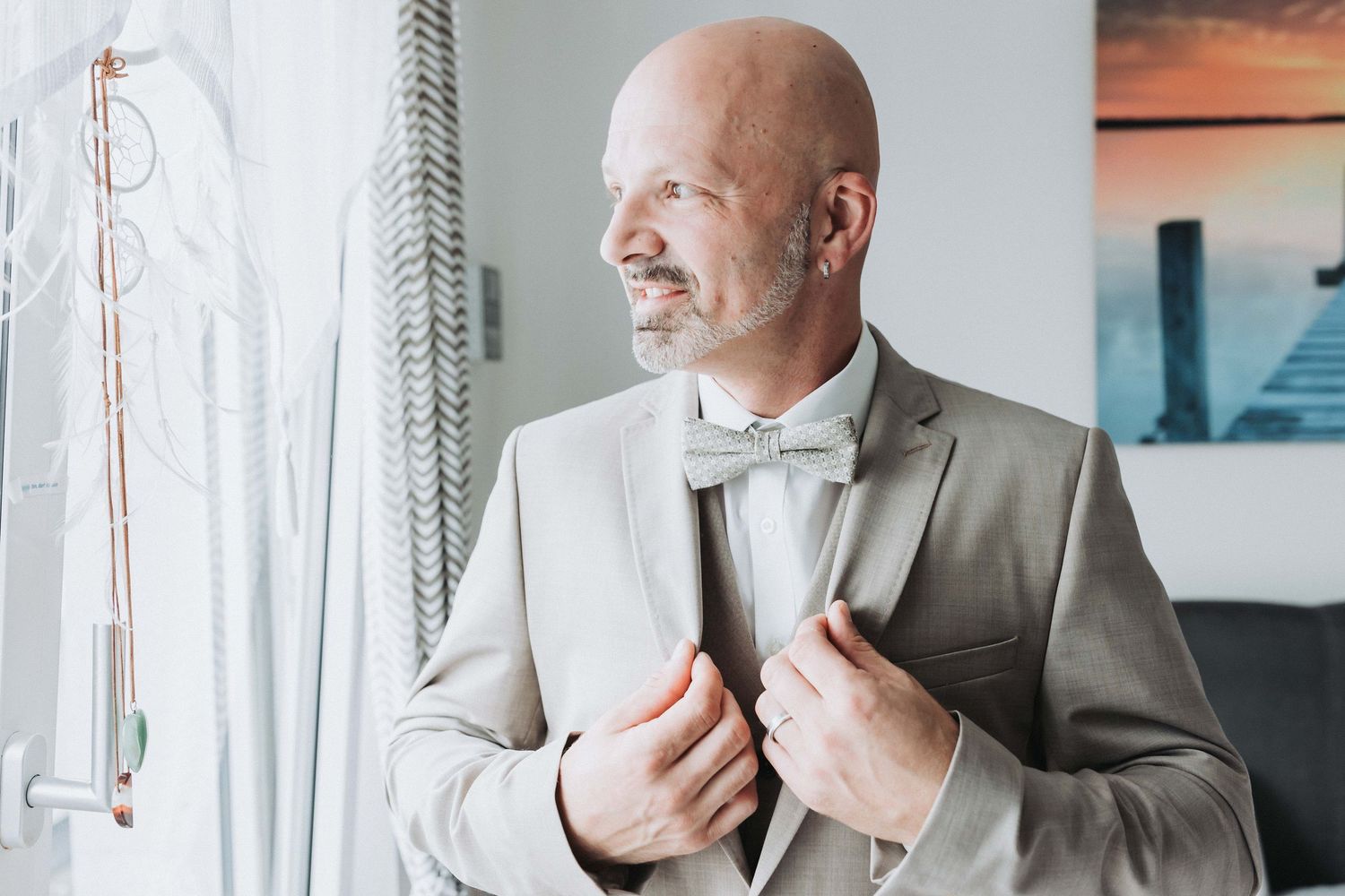 Professional in a gray suit adjusts his tie while standing by large windows in a modern office setting.