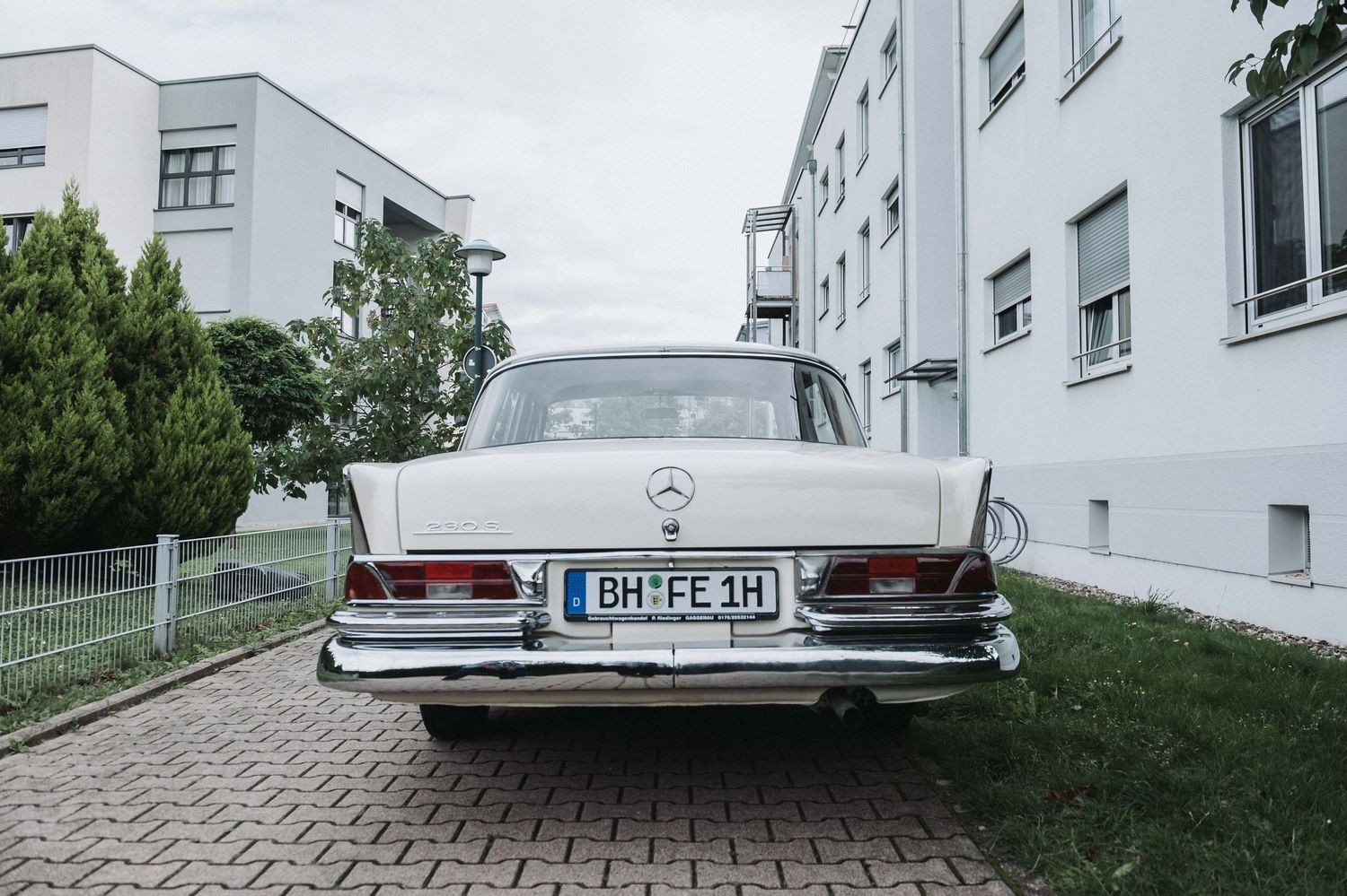 Classic white Mercedes-Benz parked on cobblestone driveway between apartment buildings.