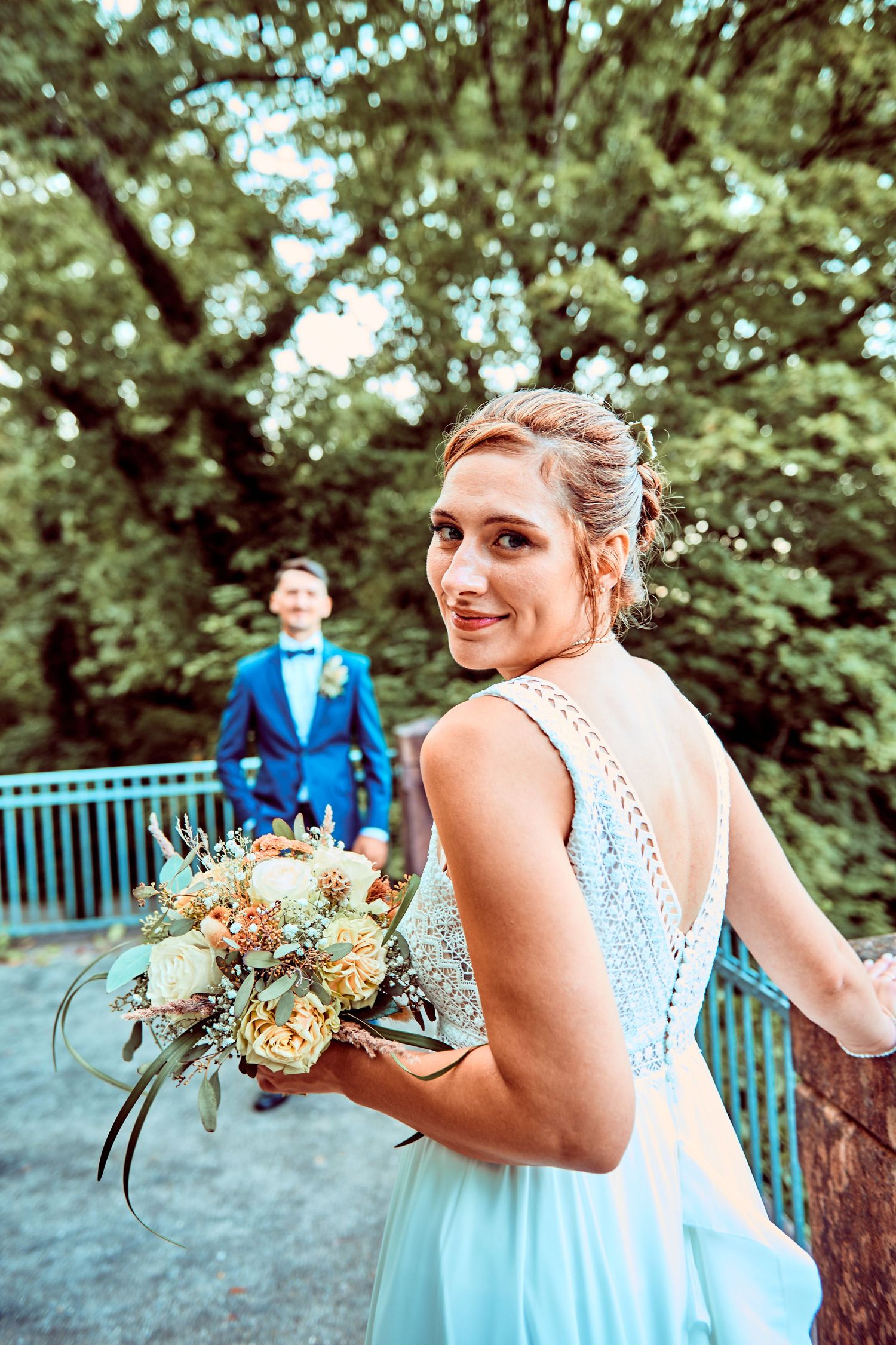 A wedding party in light blue dresses poses with peach and cream colored bouquets in a garden setting.
