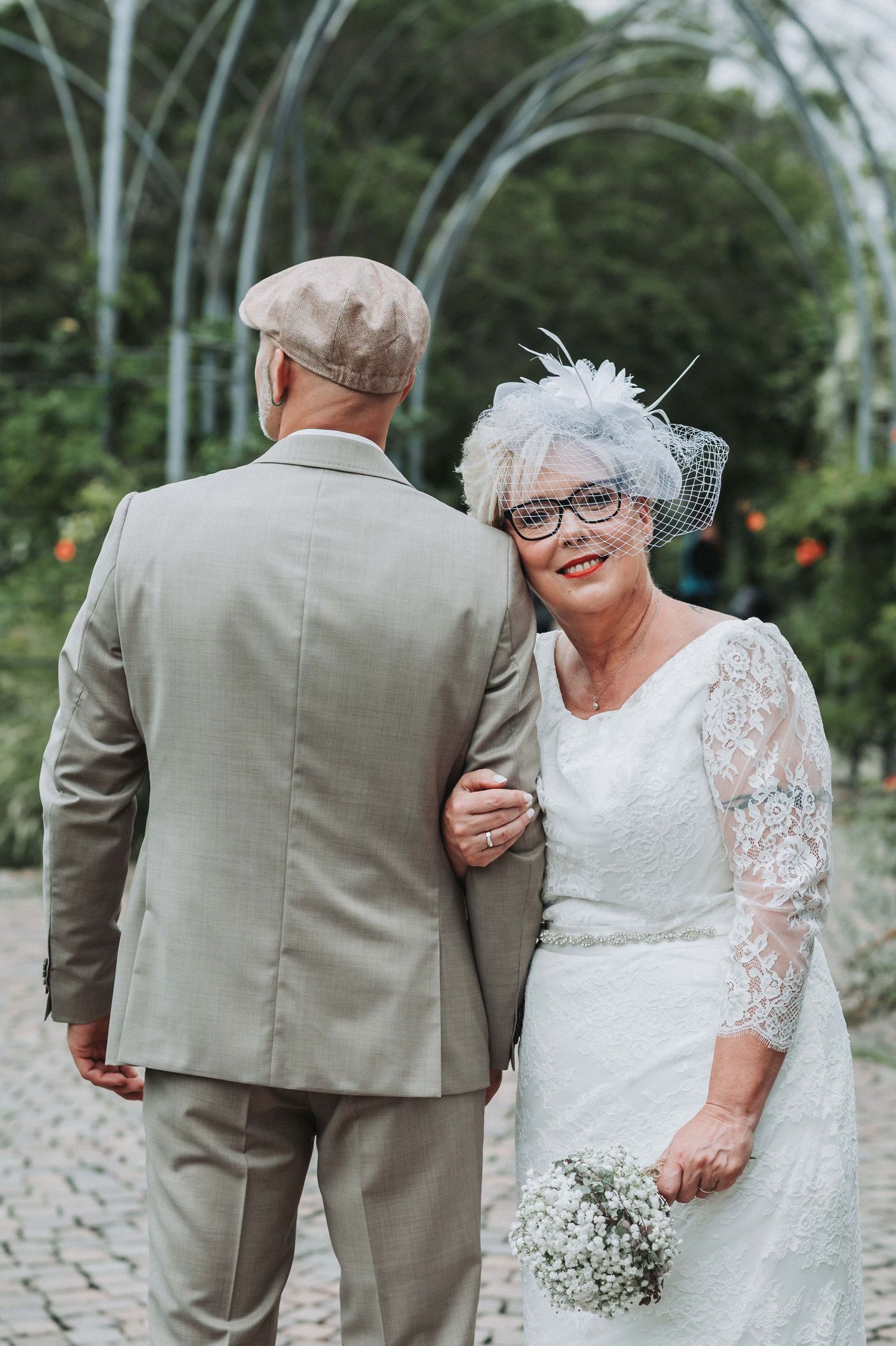 A romantic wedding photo series showing a bride in white lace and groom in tan suit walking together outdoors.