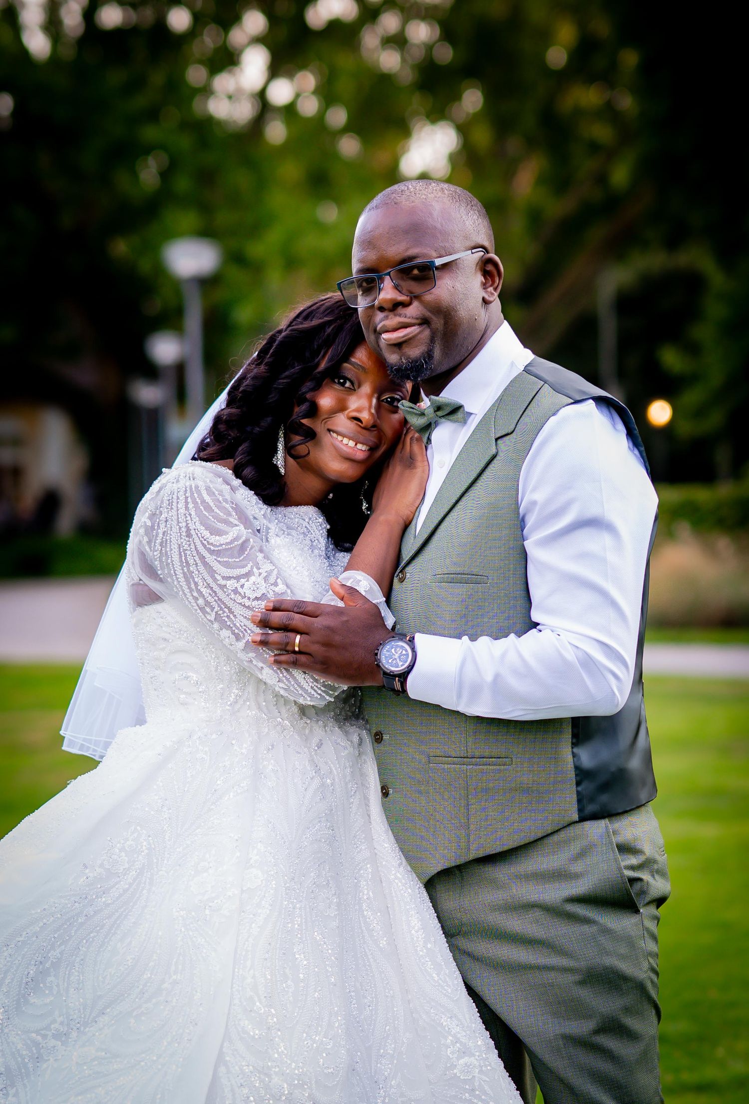 A joyful bride and groom embrace outdoors on their wedding day, wearing elegant white gown and sage green suit.
