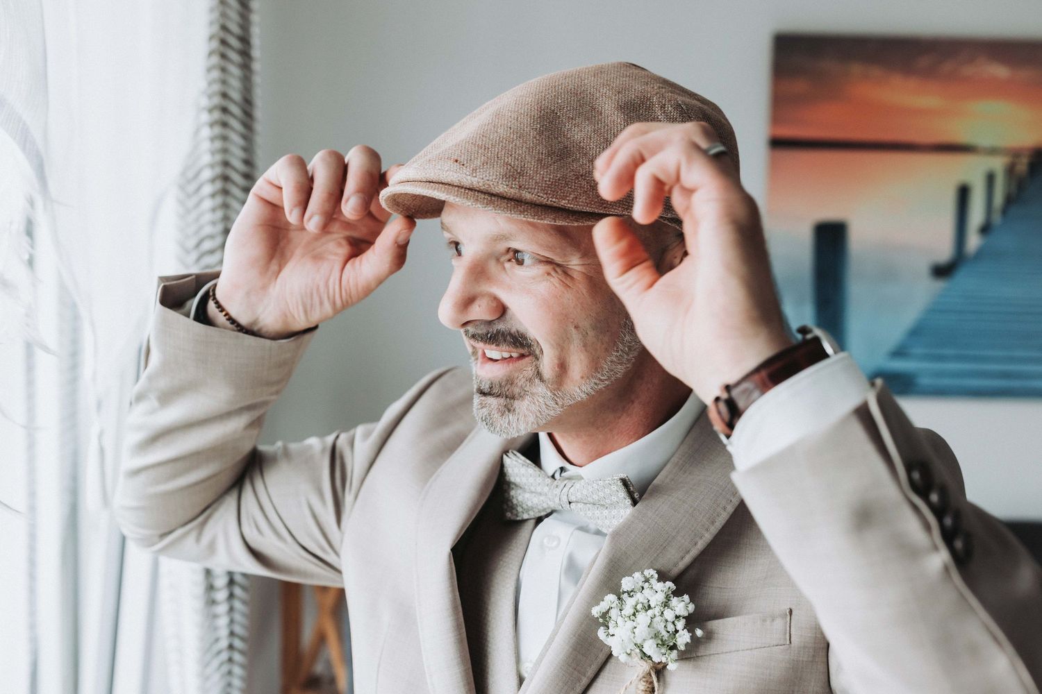 A person wearing a gray suit adjusts their tie while standing near a window with natural light.