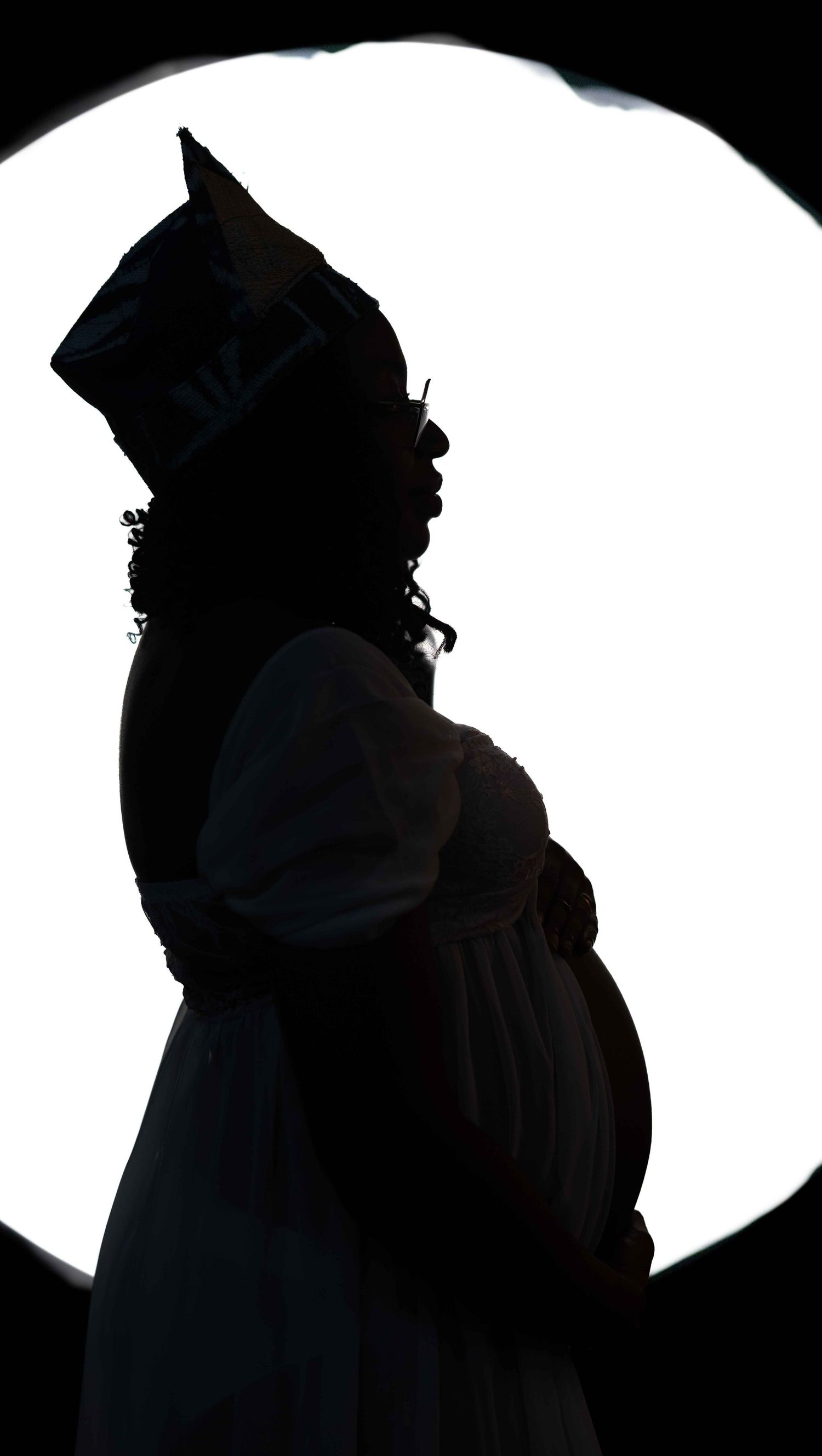 Silhouetted profile against bright white circle shows figure in hat with curly hair and flowing dress.