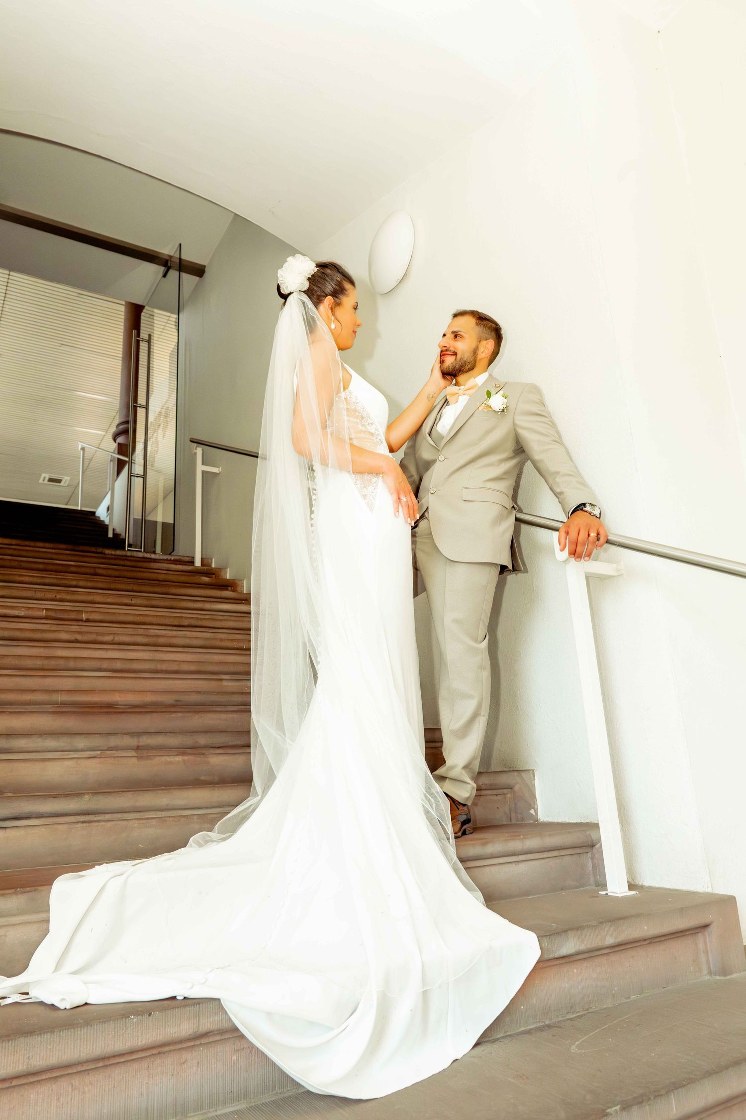 Bride and groom share an intimate moment on a staircase, with her long veil trailing behind her.