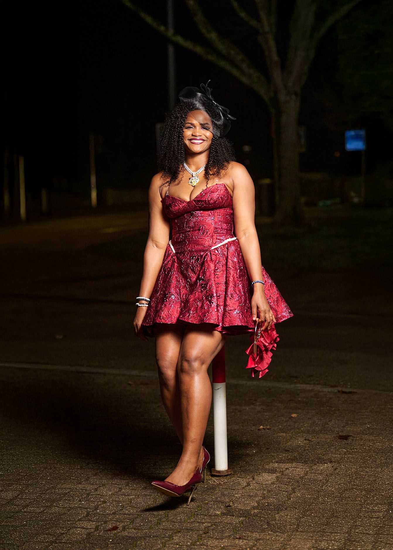 A woman in a burgundy dress poses confidently on a dark pathway at night in a series of artistic shots.