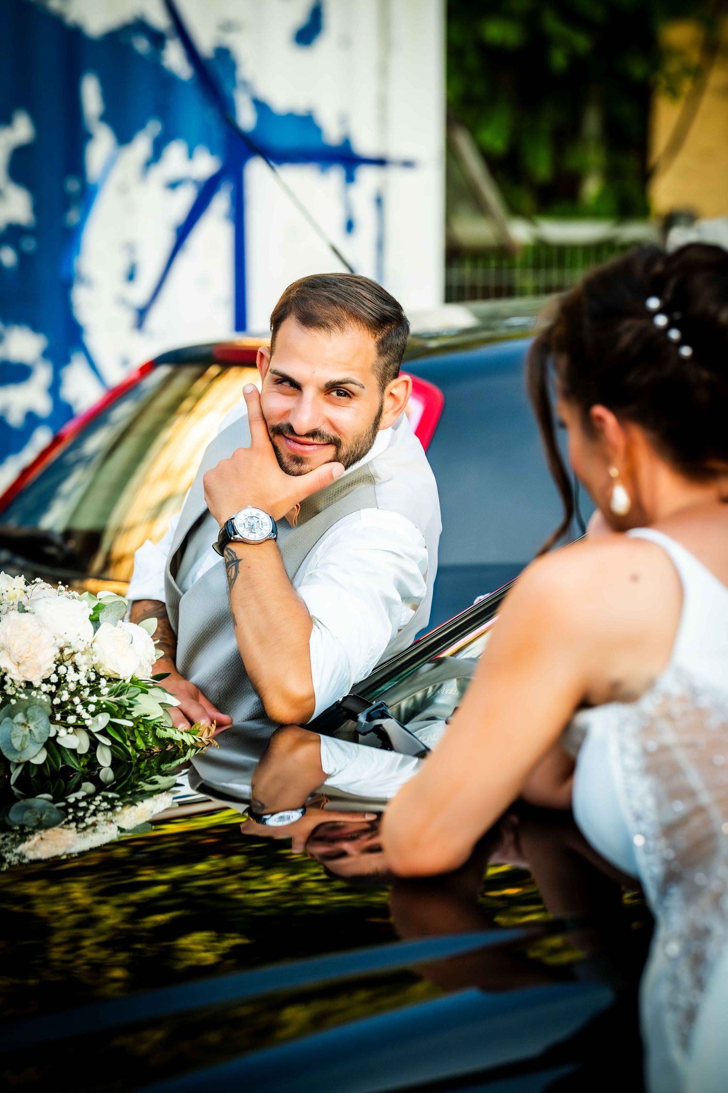 Candid moment between two people talking through a car window with white floral decorations visible.