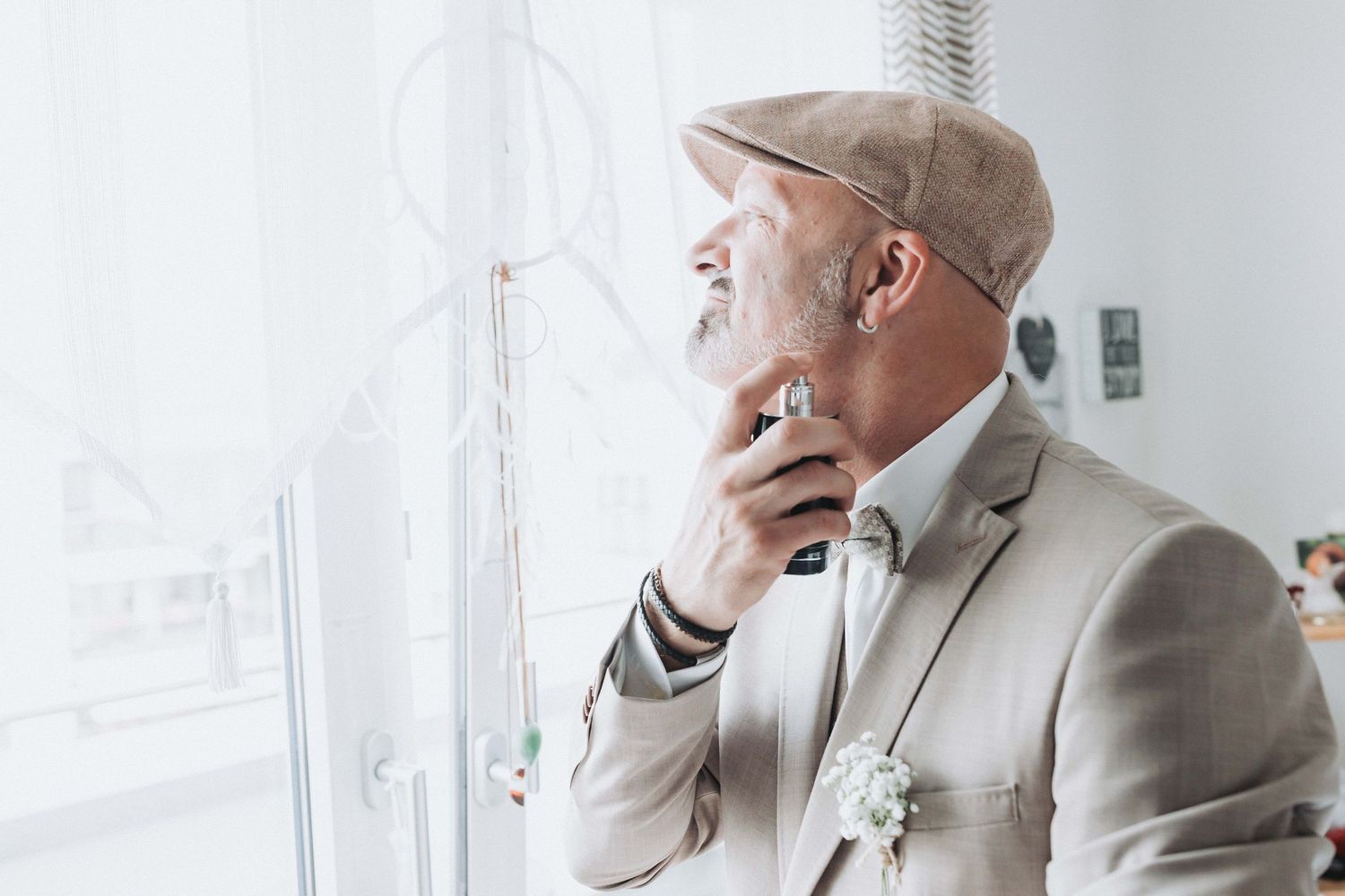 A person in a light gray suit and white shirt stands in a bright white room with modern decor.