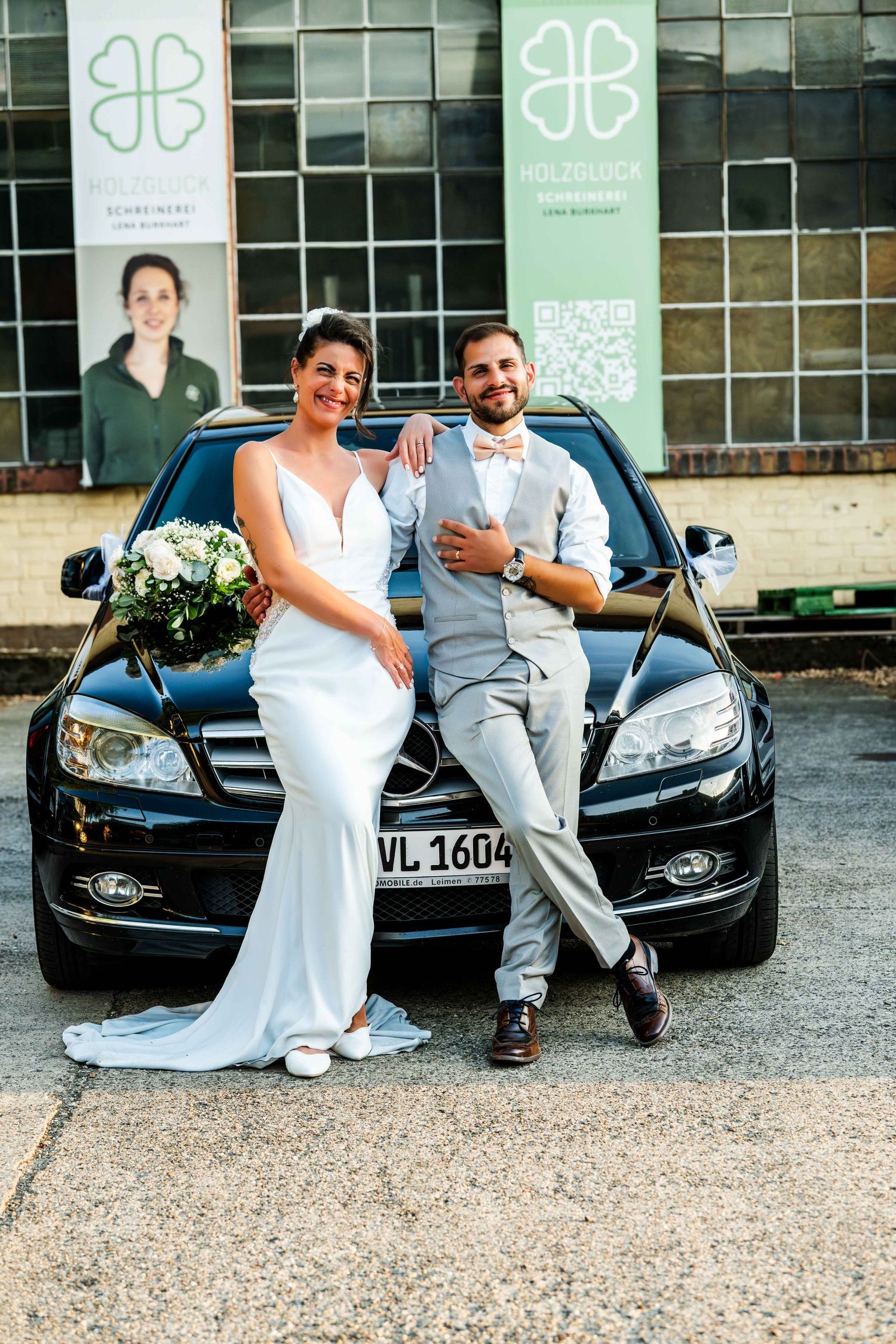 Bride and groom posing together leaning on a black Mercedes car on their wedding day.