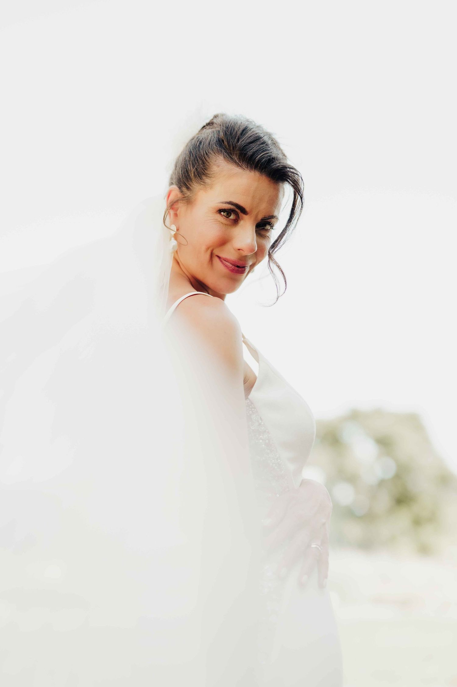 Beautiful bride in white wedding dress and veil smiling over her shoulder in an elegant portrait.