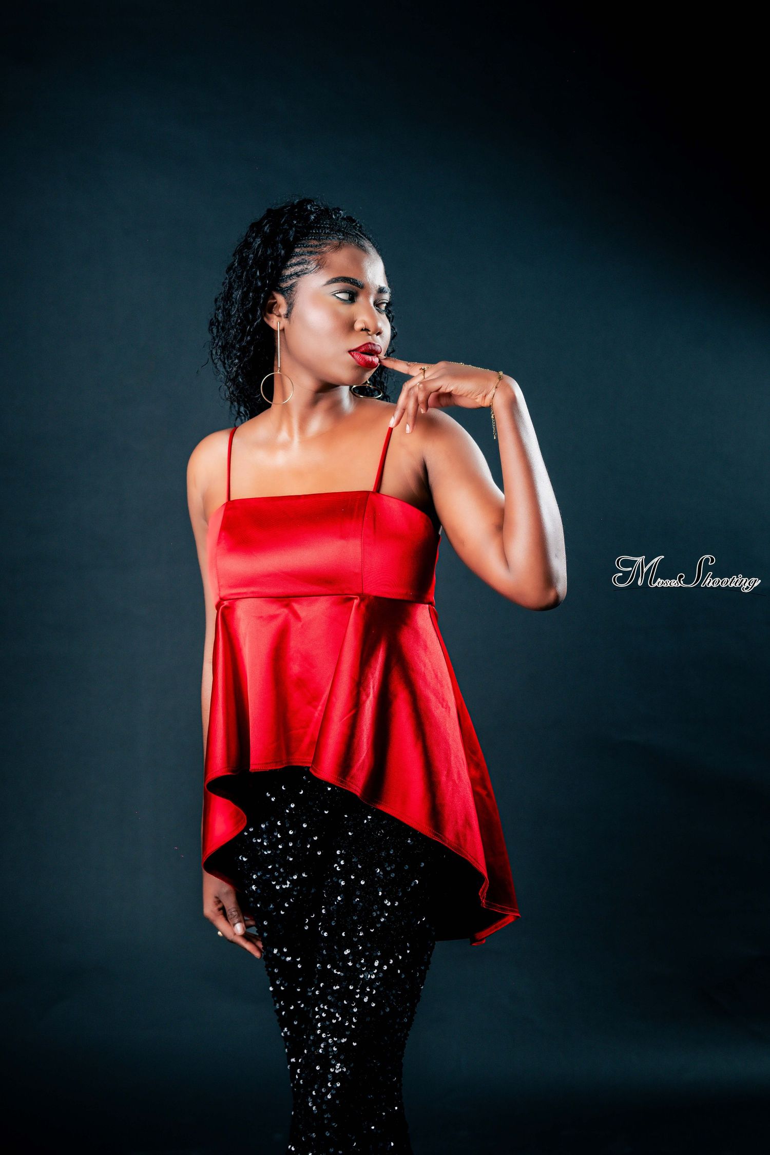 A figure in a flowing red top and sparkly black skirt poses dramatically against a dark studio backdrop.