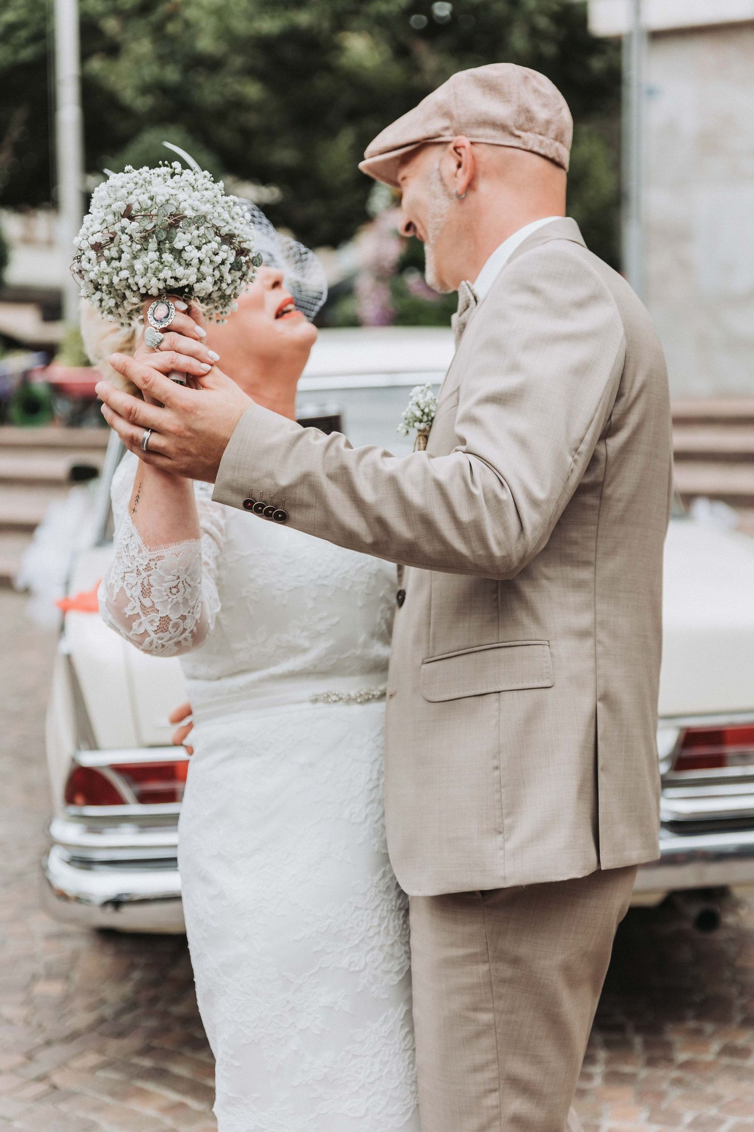 A couple in wedding attire share an intimate dance moment outdoors, with the bride in white and groom in beige.