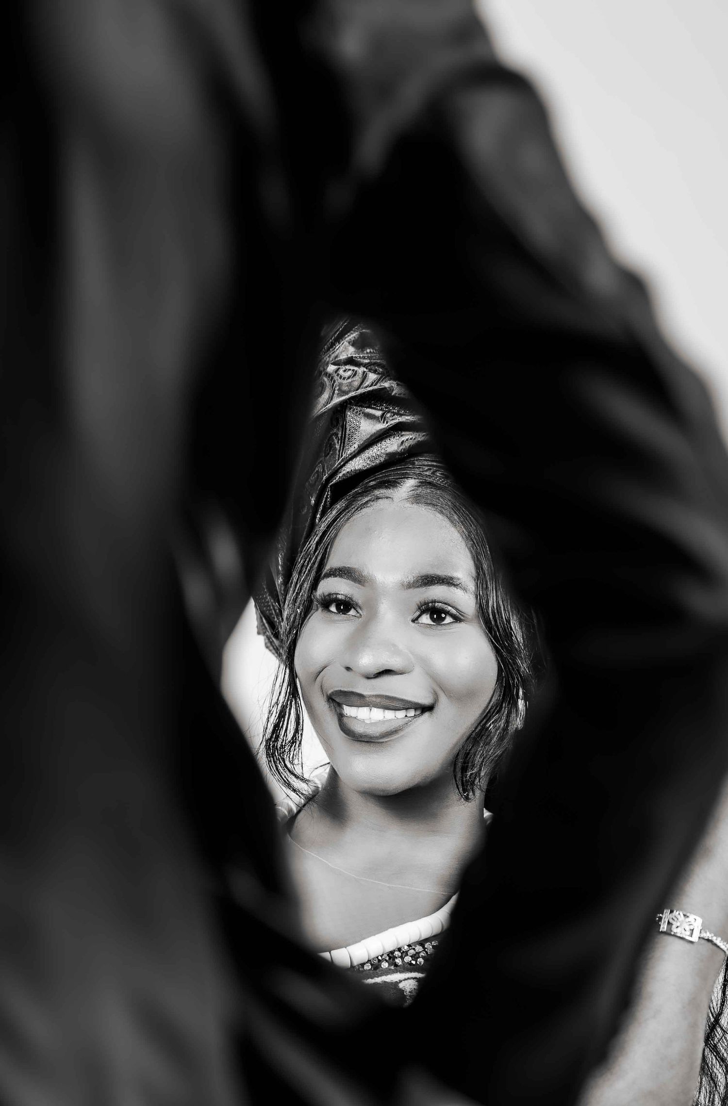 A black and white portrait photograph showing a bright smile and decorative headpiece against a dark background.