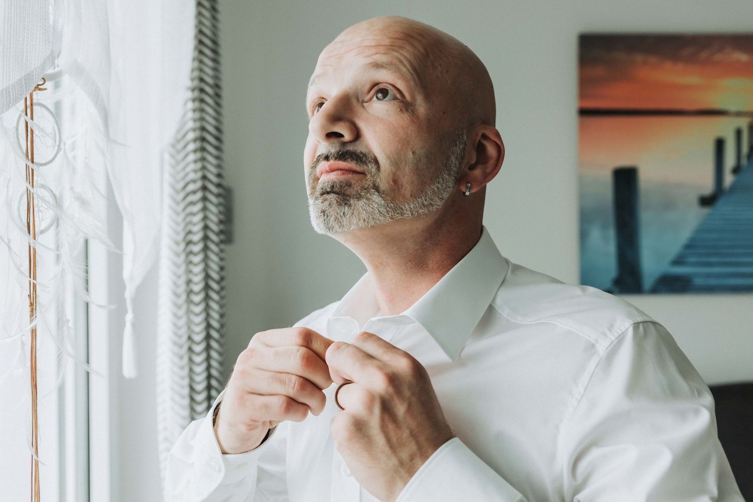 Man in white shirt looking thoughtful while standing against a wall with multiple framed artworks.