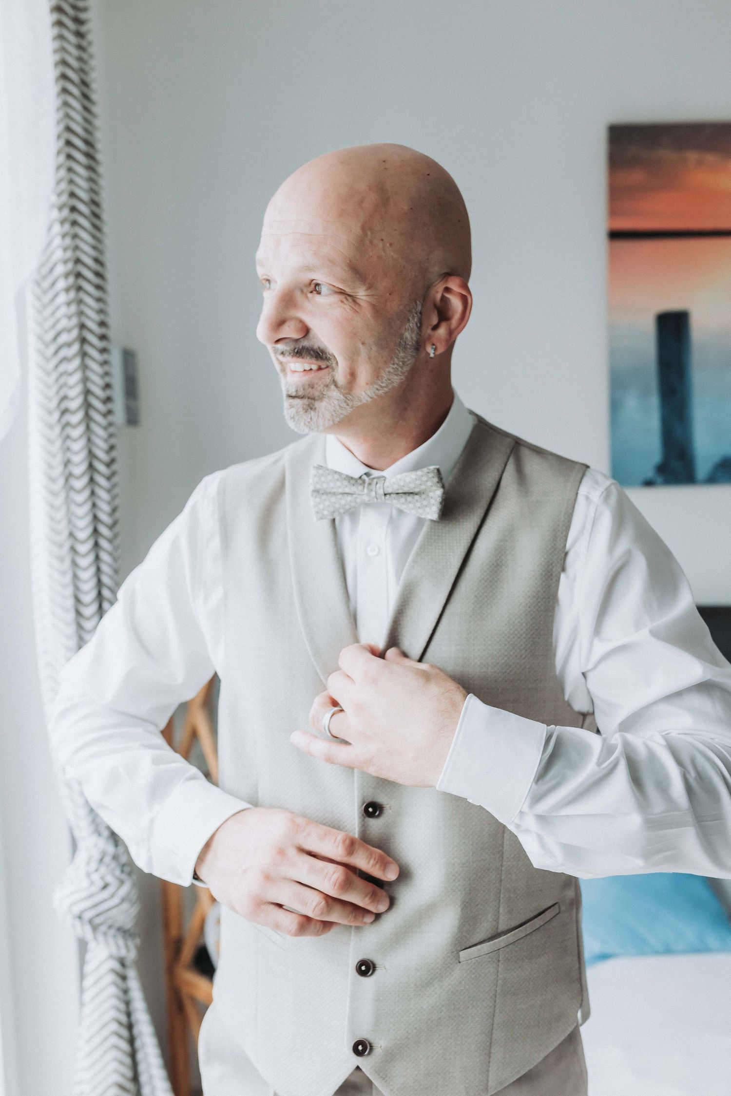 A person in a light colored suit vest adjusts their collar and tie while getting dressed in a bright interior setting.