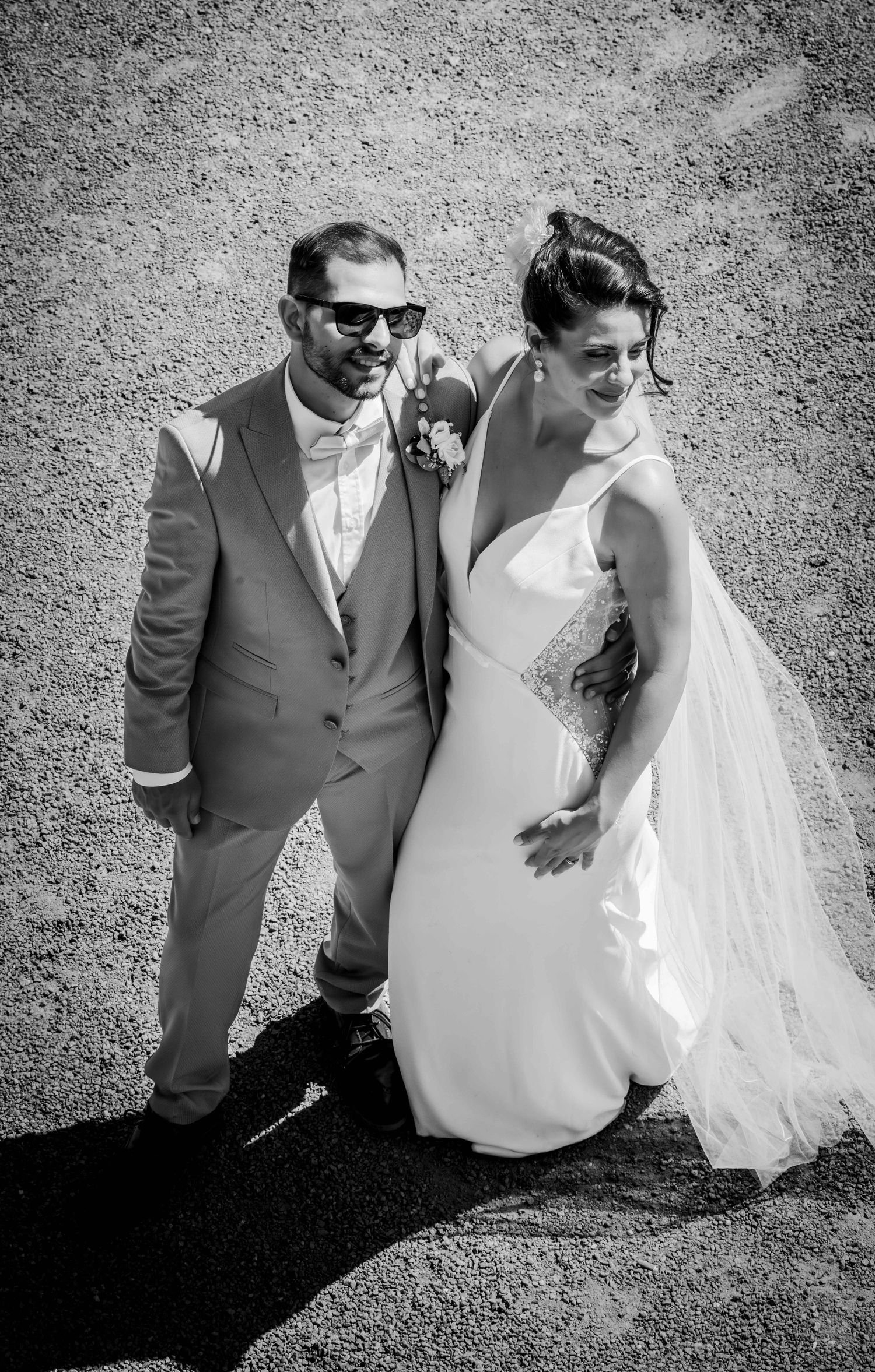 Black and white photo of a bride and groom walking together on their wedding day, groom wearing sunglasses and suit.