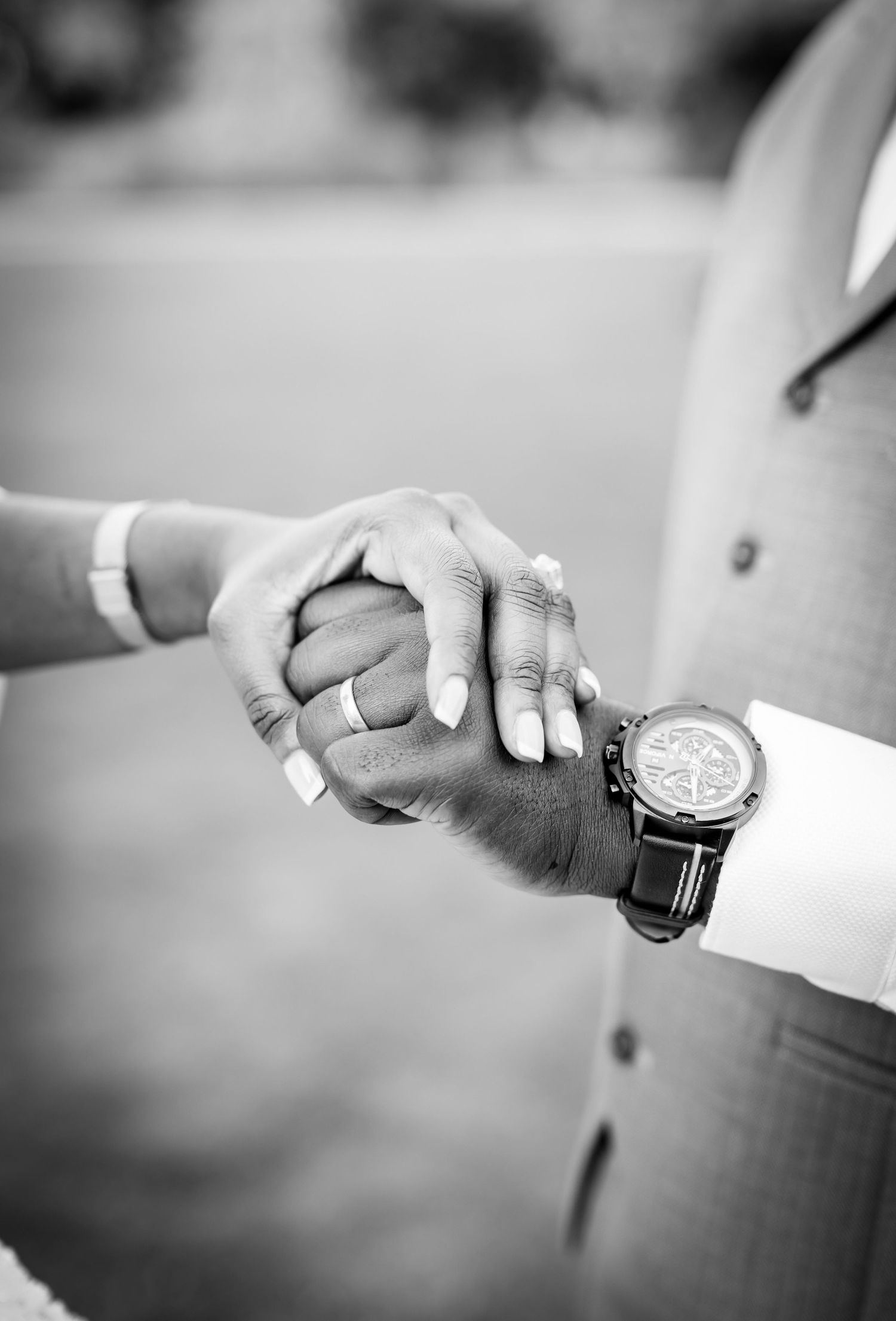 Black and white photo of a couple holding hands, showing wedding rings and a luxury watch, symbolizing marriage and love.