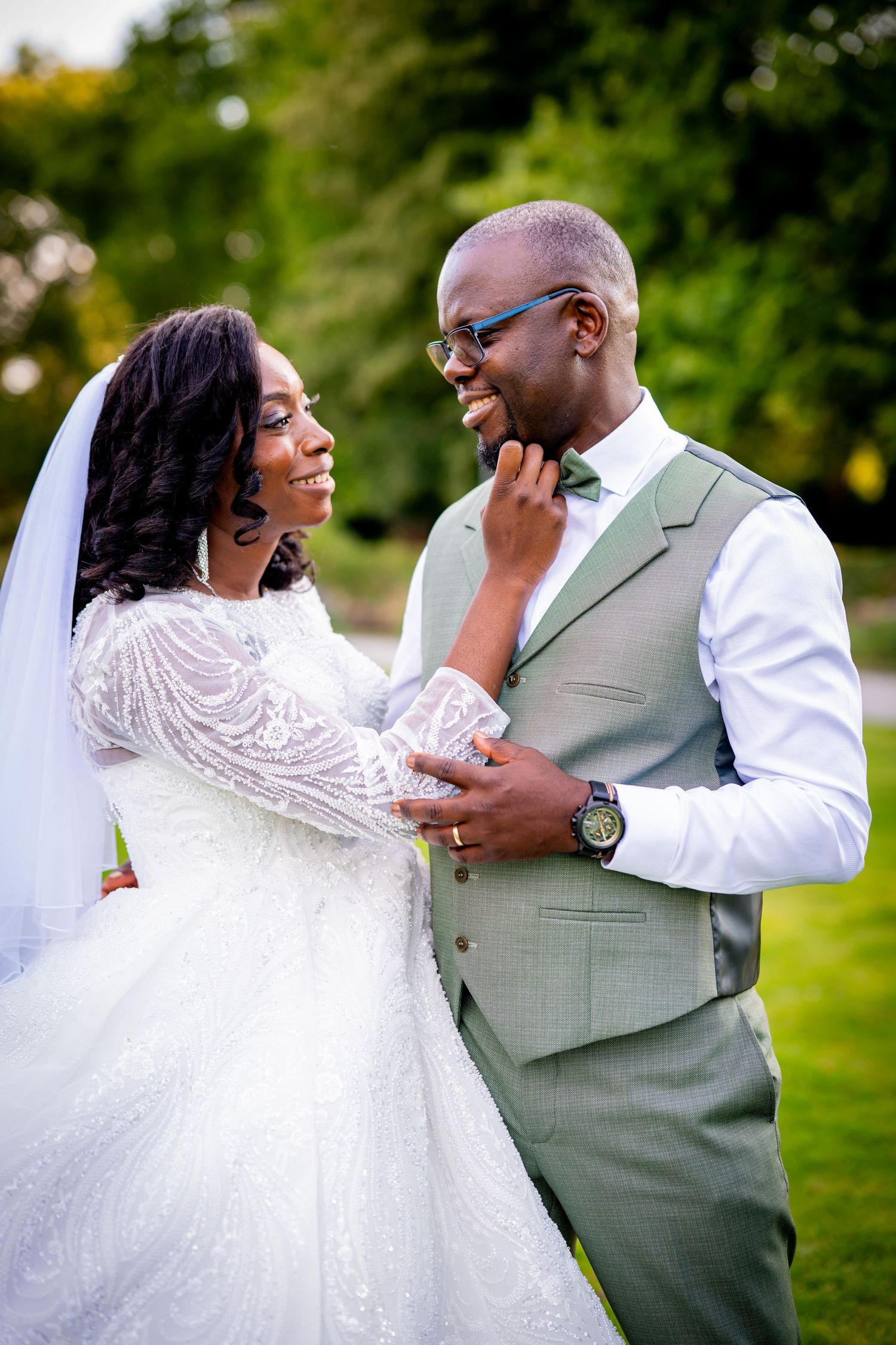 Smiling Black bride and groom in sage suit share tender moment outdoors on wedding day.