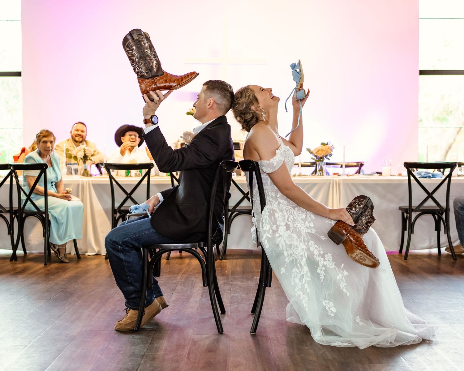 Bride and groom play the shoe game while holding cowboy boots up at their western-themed wedding reception at sorelle in Thomas, oklahoma