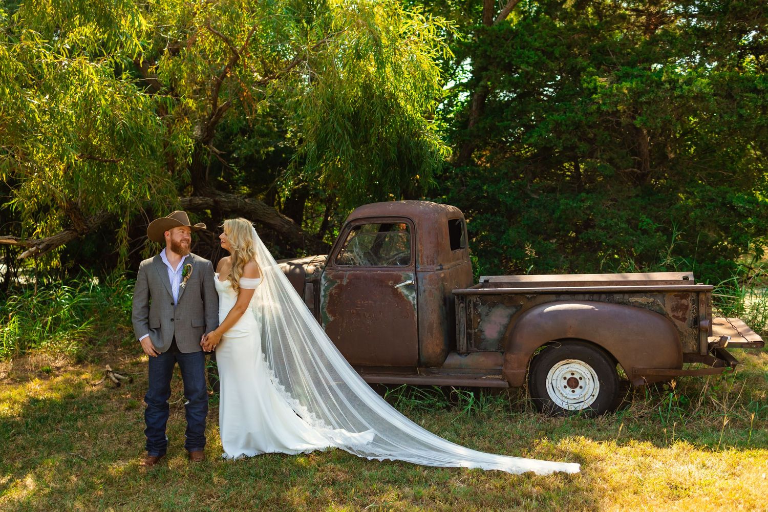 Bride and groom posing beside a rustic vintage truck outdoors on their wedding day in Guthrie Oklahoma. western wedding