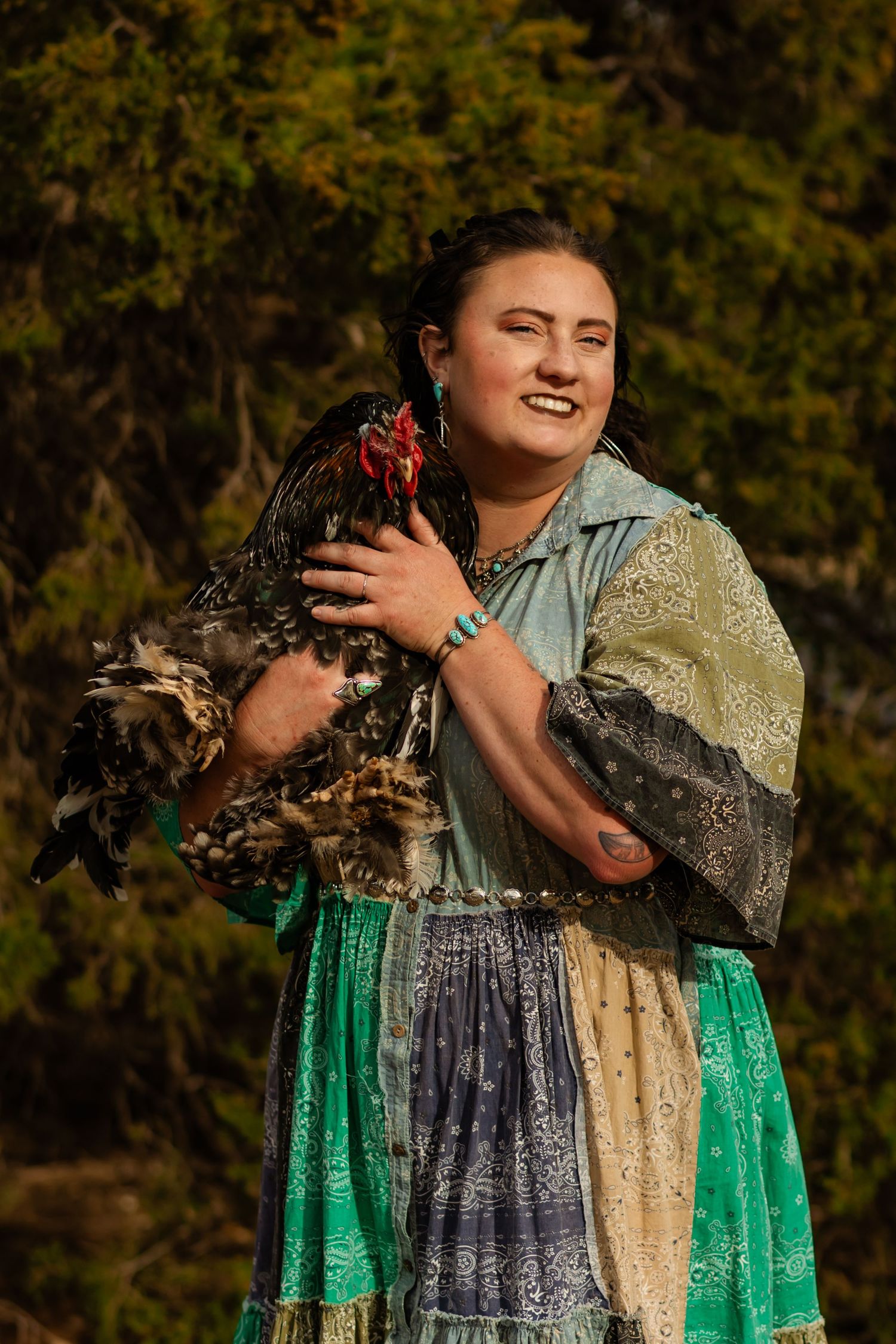 Smiling young woman in colorful patchwork dress holding a rooster outdoors. Aspynn Tabor Photography. Oklahoma photographer